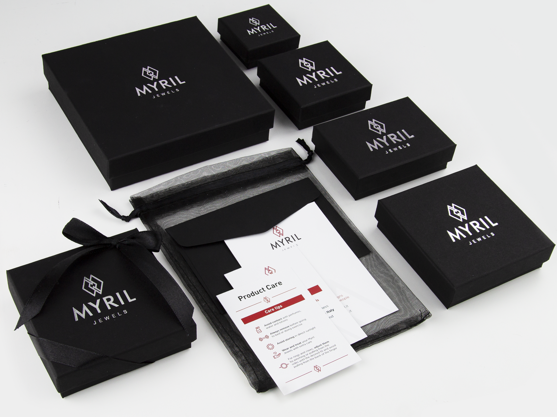 A variety of Myril Jewels brand packaging, showcasing sophisticated black boxes in multiple sizes adorned with the company's logo in silver. Included are care instructions and black organza gift bags, embodying an elegant goth jewelry presentation and branding.