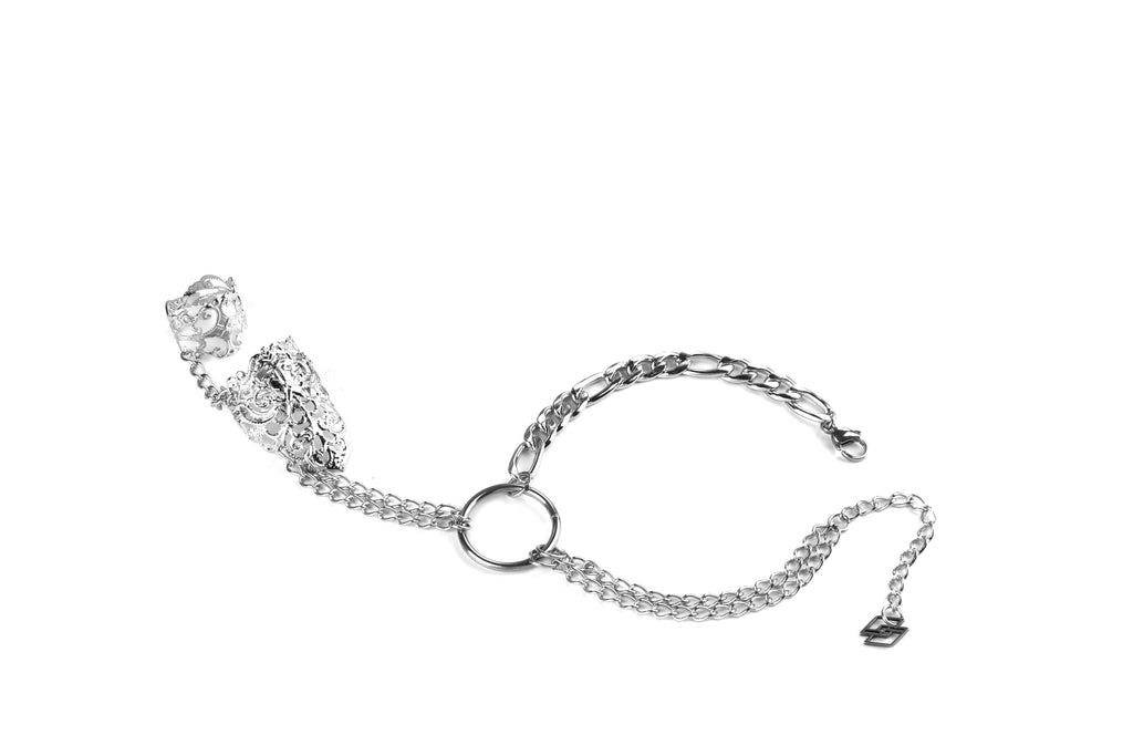 A striking Myril Jewels punk hand chain bracelet ring crafted for the modern gothic connoisseur. This elegant piece features intricate filigree detailing on the adjustable ring, seamlessly connected by a shimmering, sturdy chain to a classic wrist bracelet. The central metal loop accentuates the dark-avantgarde aesthetic, perfect for an understated yet bold statement. Ideal for everyday wear, this accessory captures the essence of minimal goth, suitable for Halloween events, rave parties