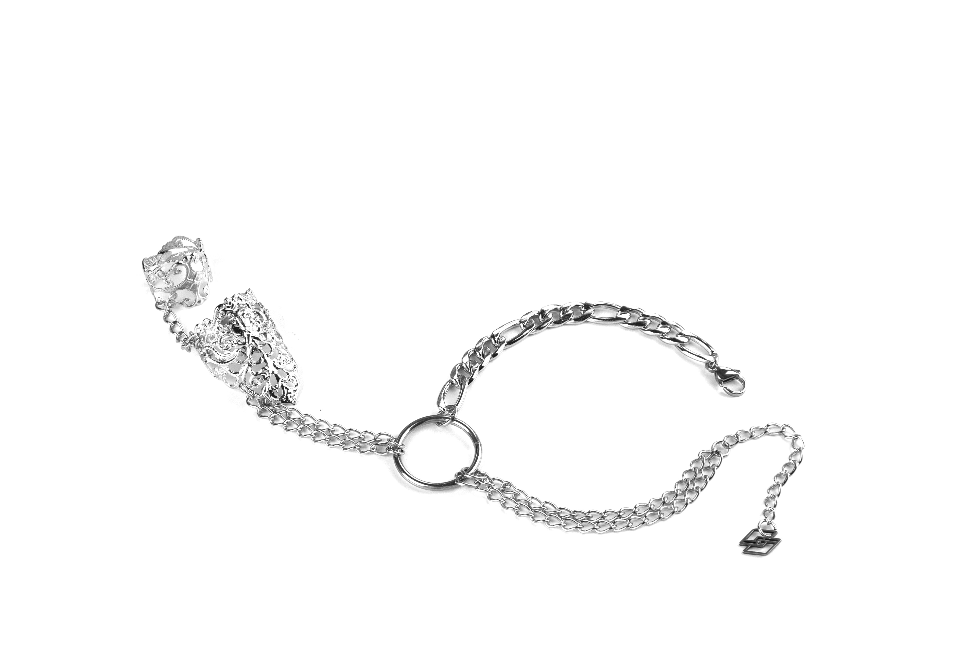 A striking Myril Jewels punk hand chain bracelet ring crafted for the modern gothic connoisseur. This elegant piece features intricate filigree detailing on the adjustable ring, seamlessly connected by a shimmering, sturdy chain to a classic wrist bracelet. The central metal loop accentuates the dark-avantgarde aesthetic, perfect for an understated yet bold statement. Ideal for everyday wear, this accessory captures the essence of minimal goth, suitable for Halloween events, rave parties