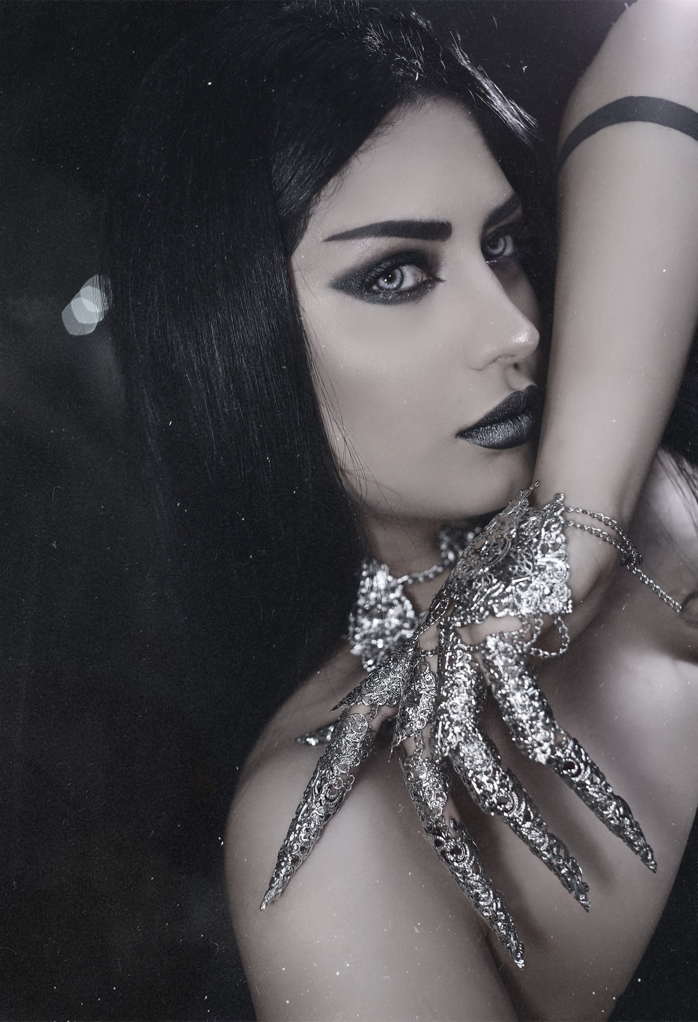 An enigmatic model (Mahafsoun) with striking black hair and makeup showcases Myril Jewels' dark-avantgarde jewelry, a perfect blend of gothic-chic and witchcore styles. The intricate silver finger armor rings create a neo-gothic statement, ideal for punk fashion or a Halloween centerpiece, embodying the brand's unique vision for alternative luxury.