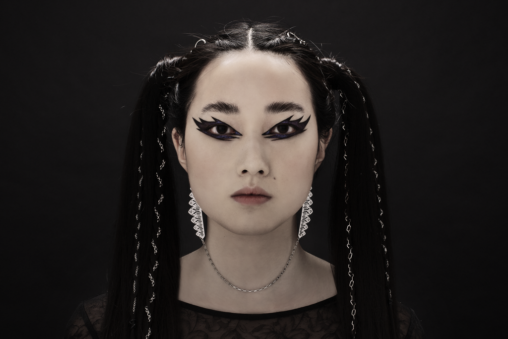 This distinctive single-piece Myril Jewels earring, with an intricate silver design, spans from one ear to the other with a delicate connecting chain. It embodies the essence of neo-gothic elegance, making it an ideal accessory for minimal goth everyday wear, or as a standout piece for rave parties. This earring captures the gothic-chic trend and is a unique gift idea for those with a love for bold, alternative jewelry