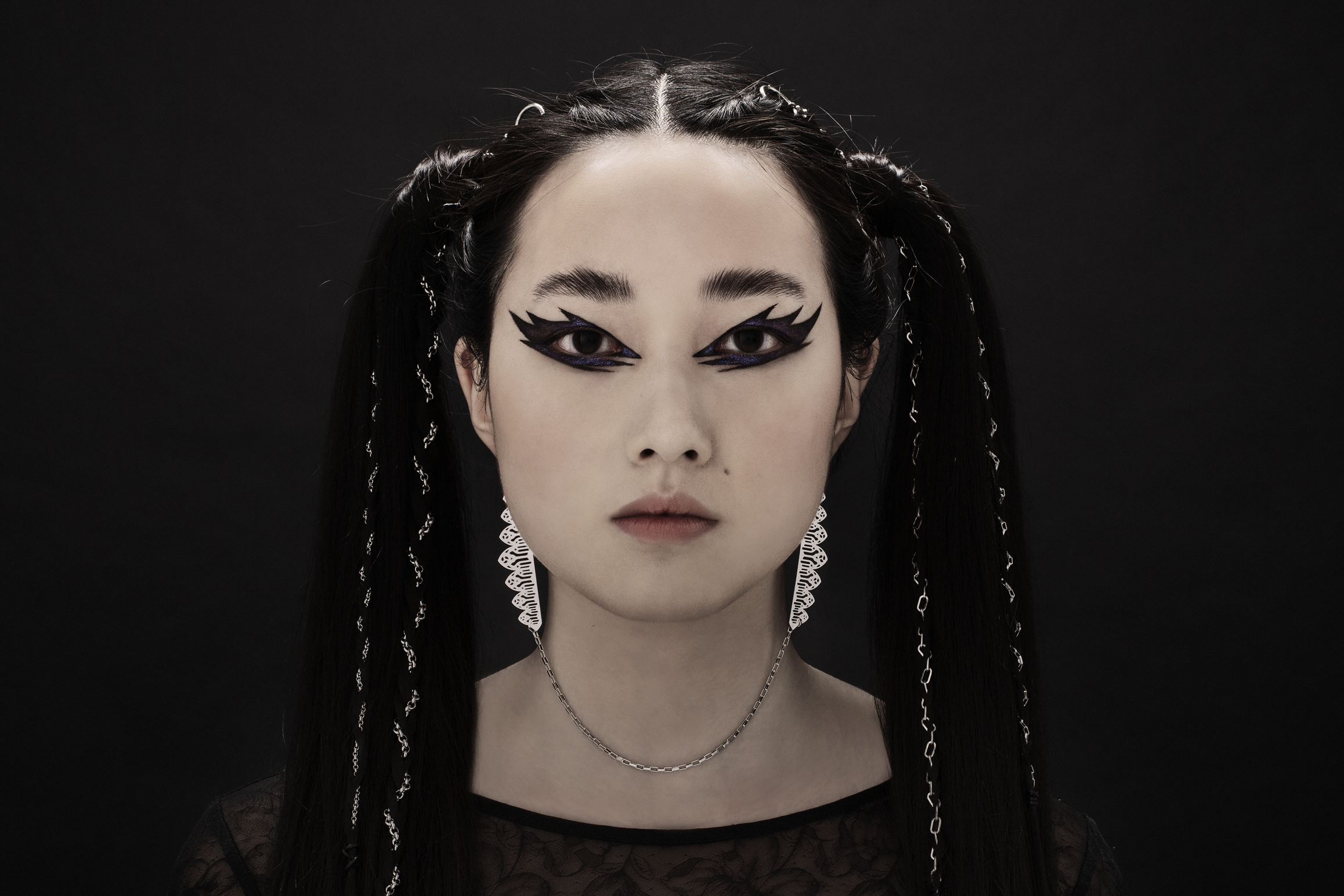 This distinctive single-piece Myril Jewels earring, with an intricate silver design, spans from one ear to the other with a delicate connecting chain. It embodies the essence of neo-gothic elegance, making it an ideal accessory for minimal goth everyday wear, or as a standout piece for rave parties. This earring captures the gothic-chic trend and is a unique gift idea for those with a love for bold, alternative jewelry