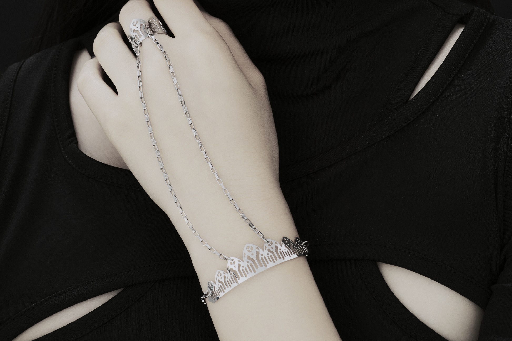 This Myril Jewels hand chain bracelet ring exudes gothic elegance, featuring a design inspired by the pointed arches of Gothic architecture. The bracelet encircles the wrist with a delicate yet bold chain, leading to a detailed ring that crowns the finger with a silhouette of arches, embodying the Neo-Gothic aesthetic. Crafted for the dark-avantgarde enthusiast, it's a versatile piece that complements both everyday minimal goth looks and elaborate festival or rave party outfits.