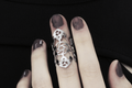 A model wears a Myril Jewels gothic architecture-inspired midi ring on her middle finger, complementing her dark manicure and black, cut-out shoulder top. The ring's intricate design and silver finish echo the sophisticated, dark-avantgarde style, perfect for fans of neo-gothic and gothic-chic jewelry. This piece blends seamlessly with a witchcore aesthetic, making it suitable for Halloween, everyday wear, and as a distinctive accessory for rave parties and festivals.