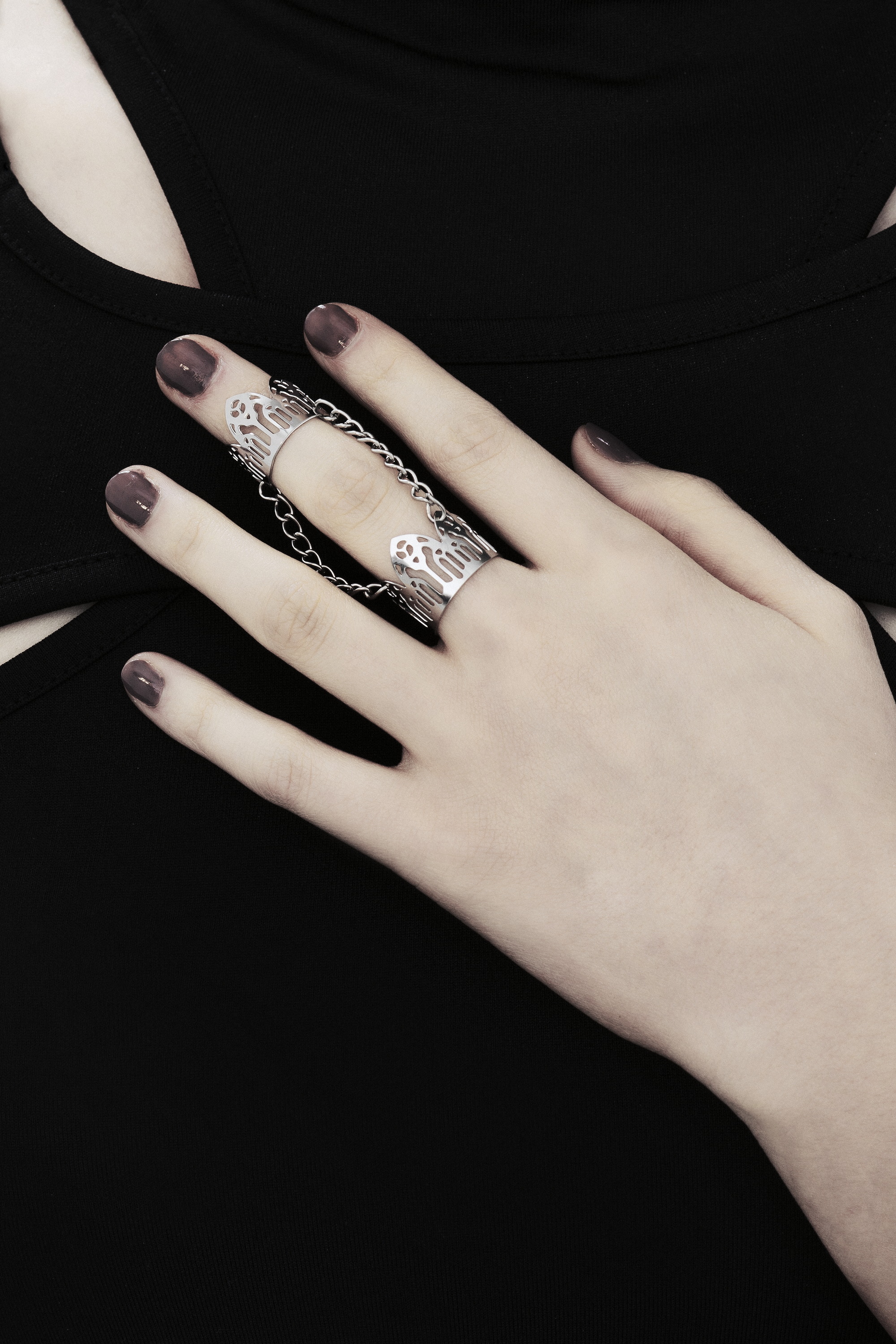 A model's hand is adorned with a Myril Jewels double ring, inspired by gothic arches, against a black top with cut-out details. The ring showcases the brand's dark-avantgarde style, ideal for gothic and alternative fashion aficionados. With a design perfect for Halloween, the ring also suits everyday wear, contributing to a minimal goth look or as an accent for rave party and festival attire. It embodies the gothic-chic and whimsigoth essence, making it a unique addition to any witchcore jewelry collection