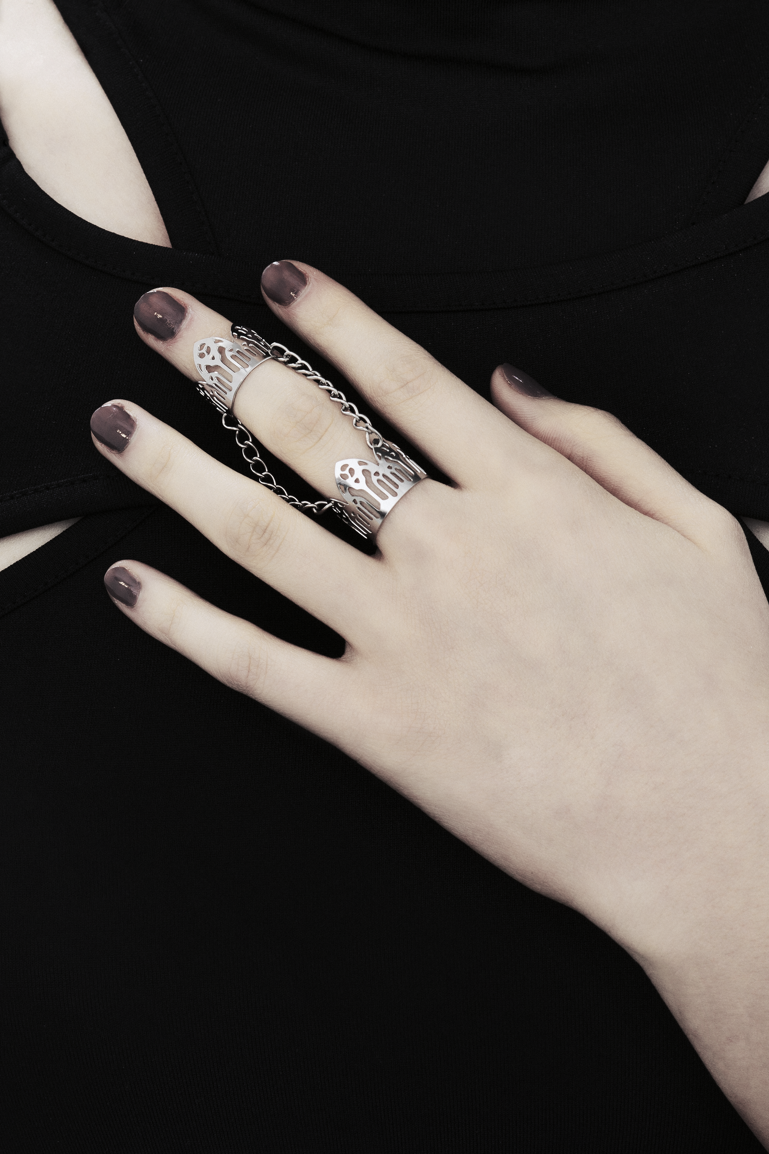 A model's hand is adorned with a Myril Jewels double ring, inspired by gothic arches, against a black top with cut-out details. The ring showcases the brand's dark-avantgarde style, ideal for gothic and alternative fashion aficionados. With a design perfect for Halloween, the ring also suits everyday wear, contributing to a minimal goth look or as an accent for rave party and festival attire. It embodies the gothic-chic and whimsigoth essence, making it a unique addition to any witchcore jewelry collection