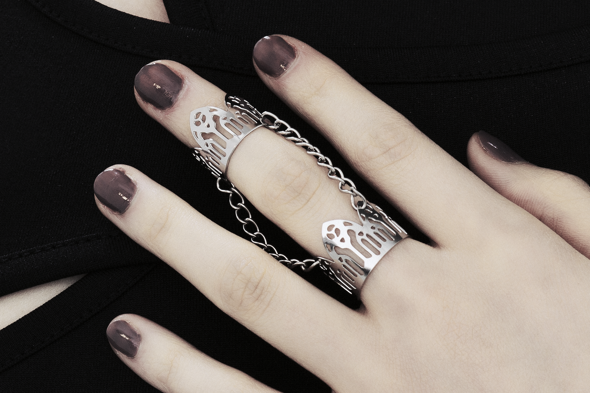 A close up image featuring a hand adorned with a Myril Jewels gothic arches inspired double ring. The ring, embodying dark-avantgarde and neo-gothic styles, wraps elegantly around two fingers, reflecting the brand's commitment to gothic-chic aesthetics. This unique piece is ideal for those who resonate with Halloween and punk jewelry trends, adding an edge to everyday wear, and complements a whimsigoth or witchcore wardrobe, perfect for rave party or festival occasions.