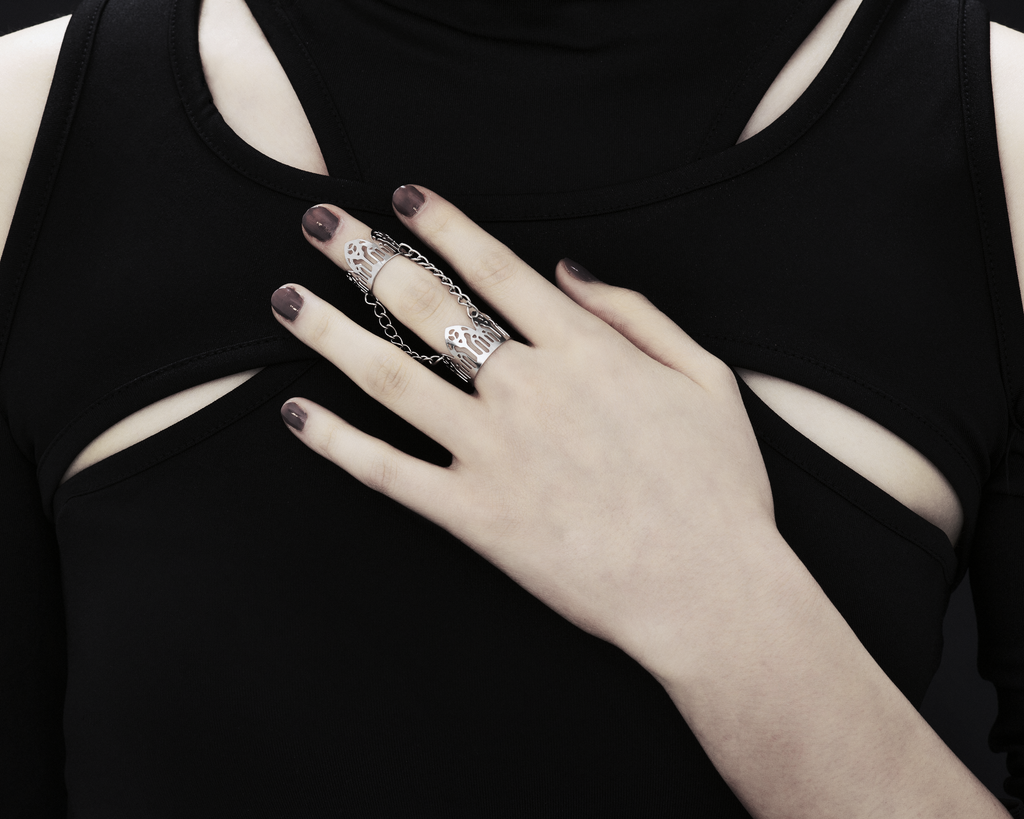 An image featuring a hand adorned with a Myril Jewels gothic arches inspired double ring. The ring, embodying dark-avantgarde and neo-gothic styles, wraps elegantly around two fingers, reflecting the brand's commitment to gothic-chic aesthetics. This unique piece is ideal for those who resonate with Halloween and punk jewelry trends, adding an edge to everyday wear, and complements a whimsigoth or witchcore wardrobe, perfect for rave party or festival occasions.