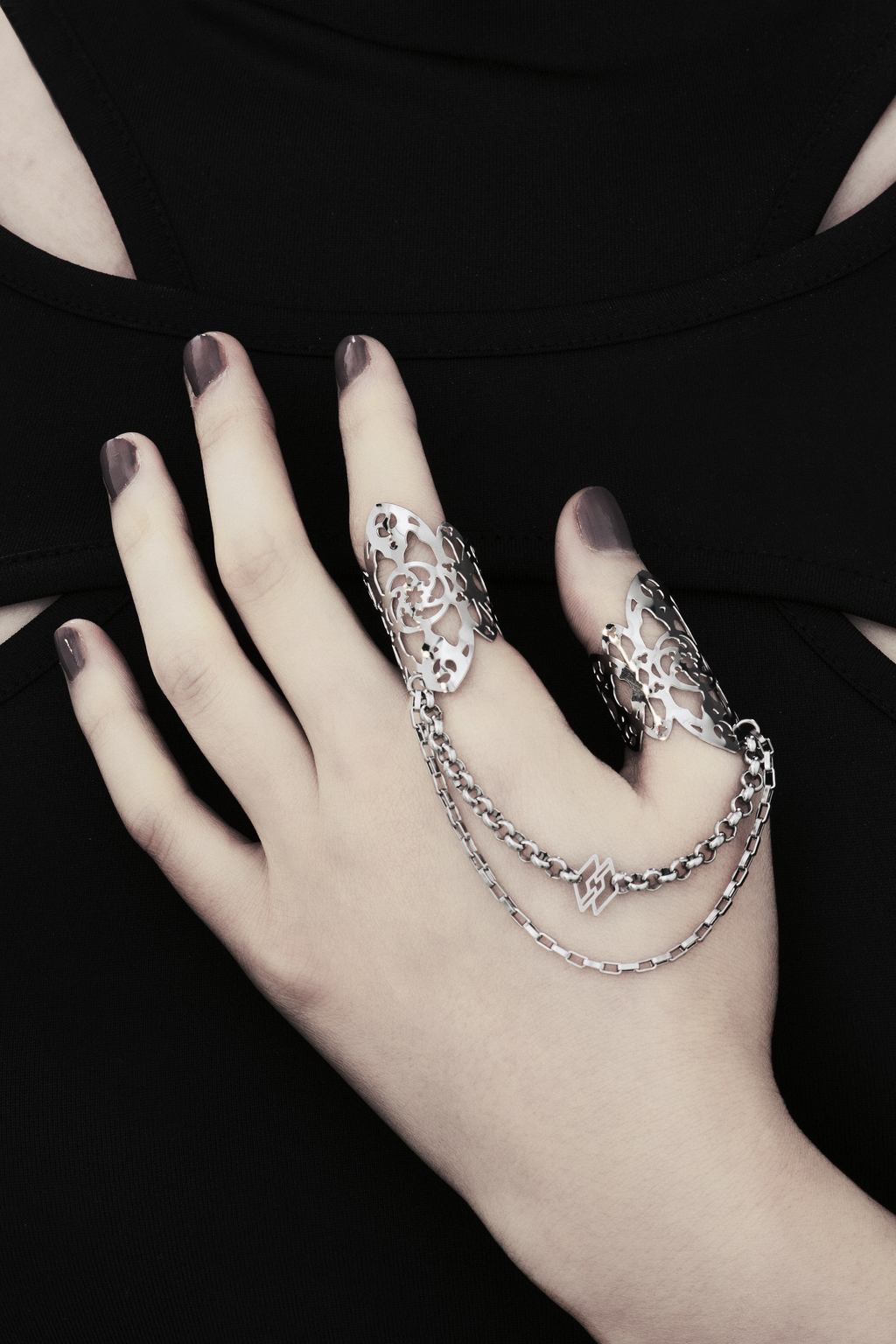 A hand models Myril Jewels' handcrafted ring featuring elaborate cut-out designs that echo a gothic architectural aesthetic, suited for lovers of dark-avantgarde fashion. The rings are interconnected with sleek chains, creating a bold, edgy look. This collection exemplifies the Italian craftsmanship and innovative style synonymous with the Myril Jewels brand, catering to the tastes of the alternative and gothic jewelry community.