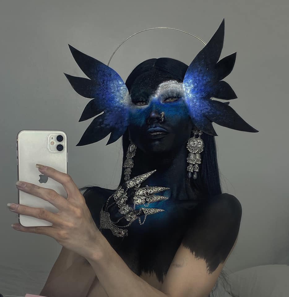 A striking self-portrait captures a model with celestial-themed makeup and dramatic winged accessories, wearing Myril Jewels' full hand silver metal glove with claw rings. This dark avant-garde makeup look is an embodiment of neo-goth jewelry, ideal for gothic, punk, and whimsigoth enthusiasts.