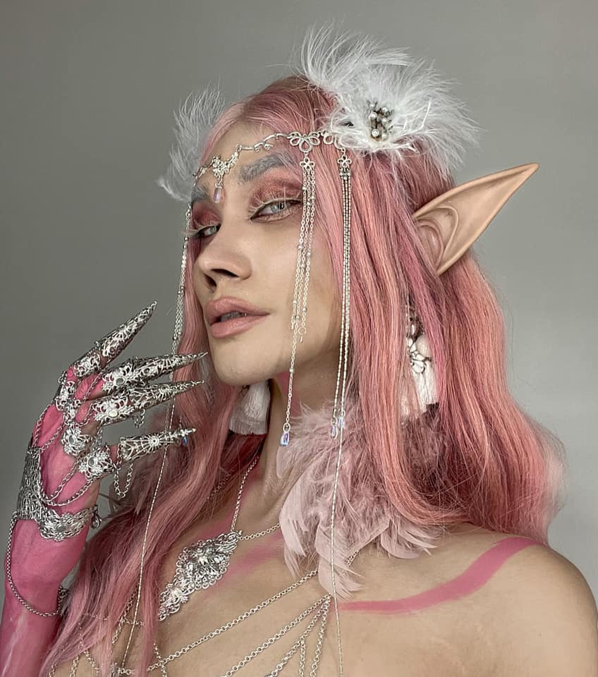 A whimsical look captures a model with pastel pink hair and elfin ears, her gaze enhanced by Myril Jewels' silver metal glove with claw rings. The ethereal makeup and neo-goth jewelry blend Whimsigoth and gothic-chic styles for a stunning, fantasy-inspired ensemble.