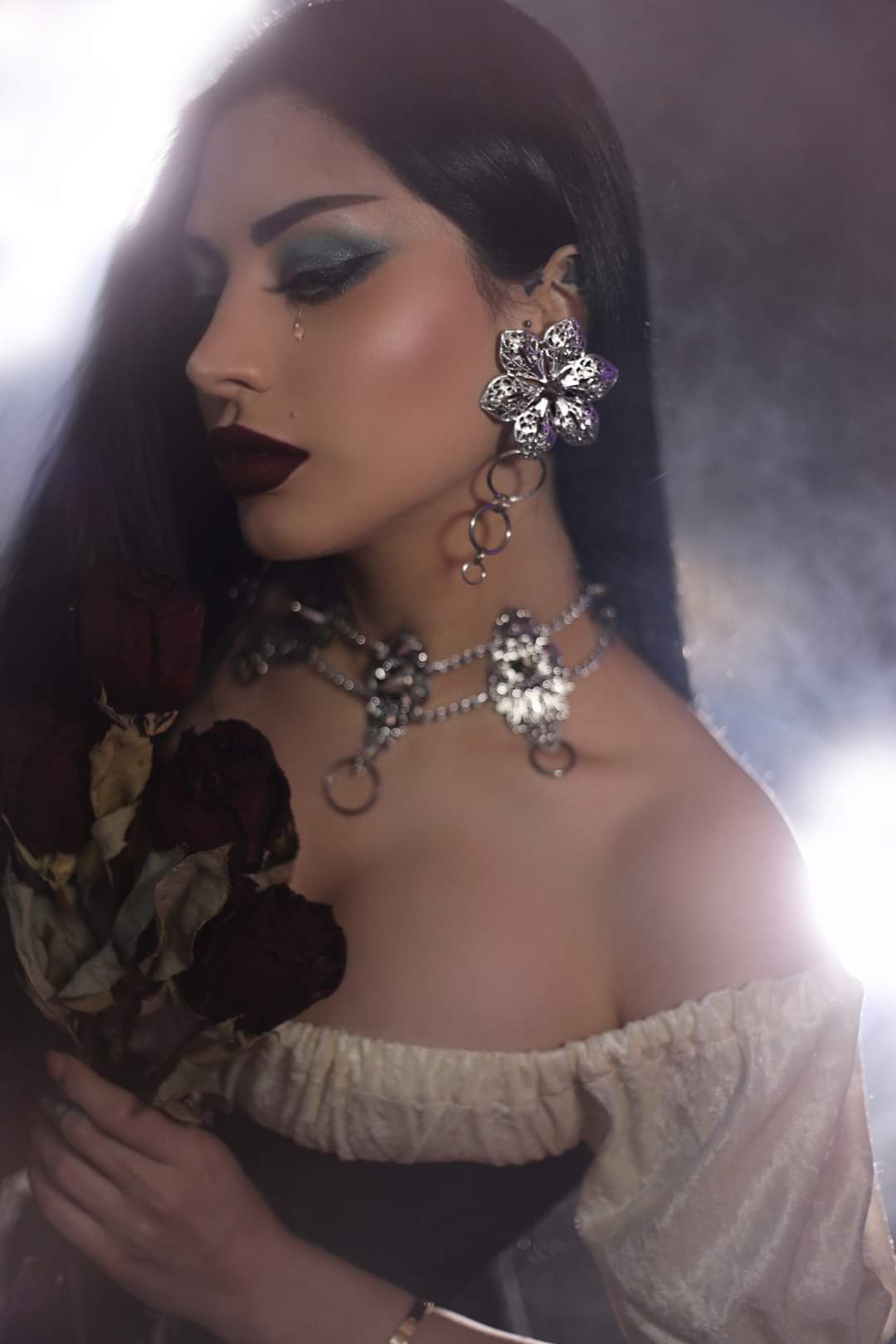 An alt model exudes dark sophistication in Myril Jewels' punk studded floral earrings and matching choker, embodying the spirit of Neo Gothic elegance. These handcrafted pieces, perfect for gothic and alternative fashion lovers, blend seamlessly with her dramatic makeup and the bouquet of dried roses she holds. Ideal for Halloween, gothic-chic events, or as a daring addition to any whimsigoth, witchcore, or minimal goth wardrobe