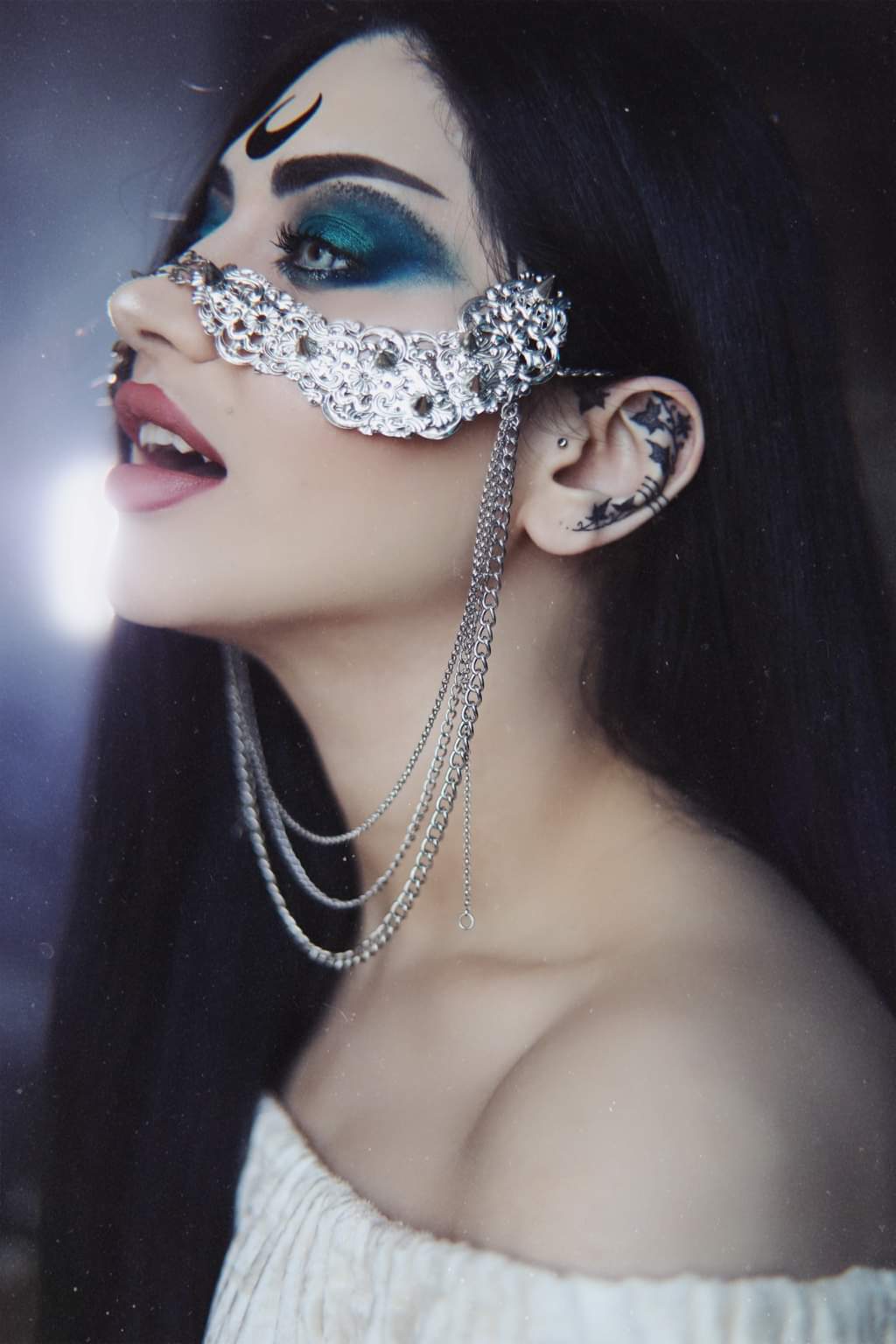 A model poses with a Myril Jewels studded nose mask, featuring a cascade of hanging chains that evoke a neo-gothic charm. This statement piece, blending punk and gothic-chic elements, exemplifies dark-avantgarde fashion. It’s a perfect accessory for those who embrace whimsigoth and witchcore aesthetics, suitable for Halloween, everyday wear, or as a standout addition to rave party and festival attire