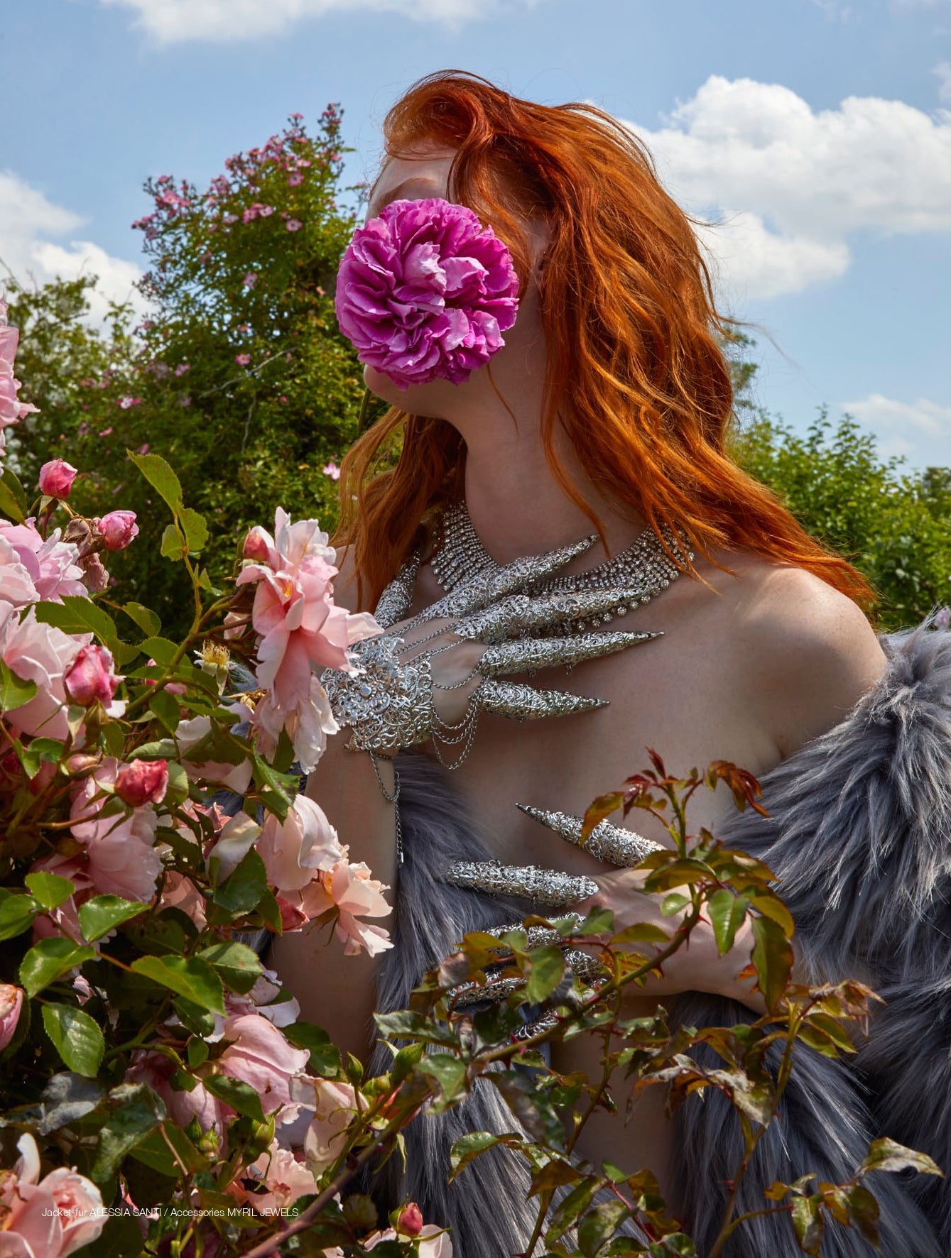 In a vibrant garden, a model with fiery red hair becomes one with nature, her face obscured by a deep pink bloom, embodying the whimsical goth aesthetic. Adorned in Myril Jewels' intricate silver metal glove with claw rings, the ensemble radiates neo-gothic elegance, perfect for gothic-chic or witchcore-inspired looks, and makes a statement piece for Halloween or punk fashion events.