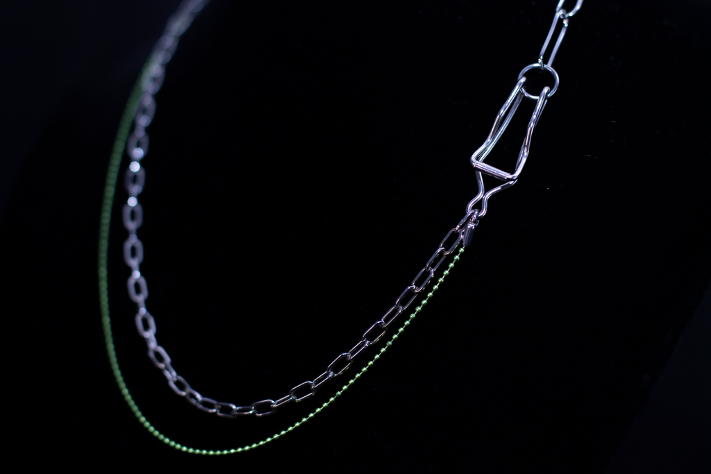 This image showcases a Myril Jewels punk silver and green chain necklace, displayed on a dark backdrop. The necklace features a contrast of sleek silver links with vibrant green accents, encapsulating the neo-goth aesthetic. It's a striking piece for those drawn to dark-avantgarde fashion, perfect for Halloween, and versatile for everyday wear, from minimal goth to the more elaborate witchcore and whimsigoth styles, as well as being suitable for rave parties and festival adornment.