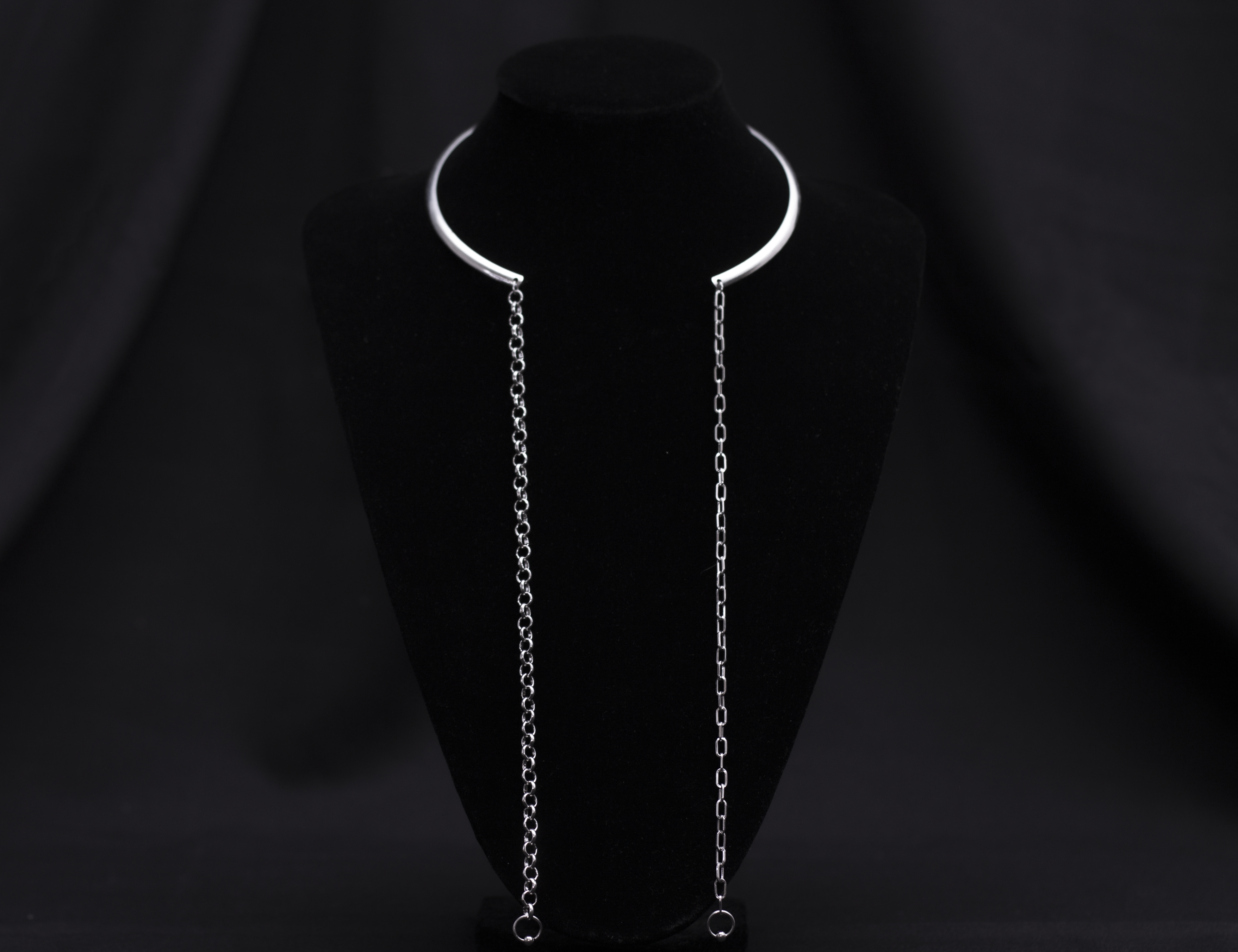  A sleek and minimal Myril Jewels necklace features a rigid, crescent-shaped neckline with long, delicate chains draping elegantly on a black velvet mannequin. This piece embodies the subtle edge of neo-gothic design, making it versatile for Witchcore enthusiasts, Halloween adornment, or as a sophisticated everyday accessory.