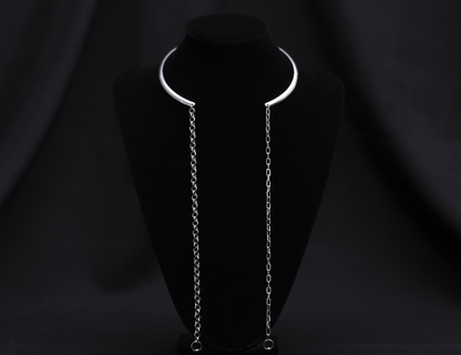 A sleek and minimal Myril Jewels necklace features a rigid, crescent-shaped neckline with long, delicate chains draping elegantly on a black velvet mannequin. This piece embodies the subtle edge of neo-gothic design, making it versatile for Witchcore enthusiasts, Halloween adornment, or as a sophisticated everyday accessory.