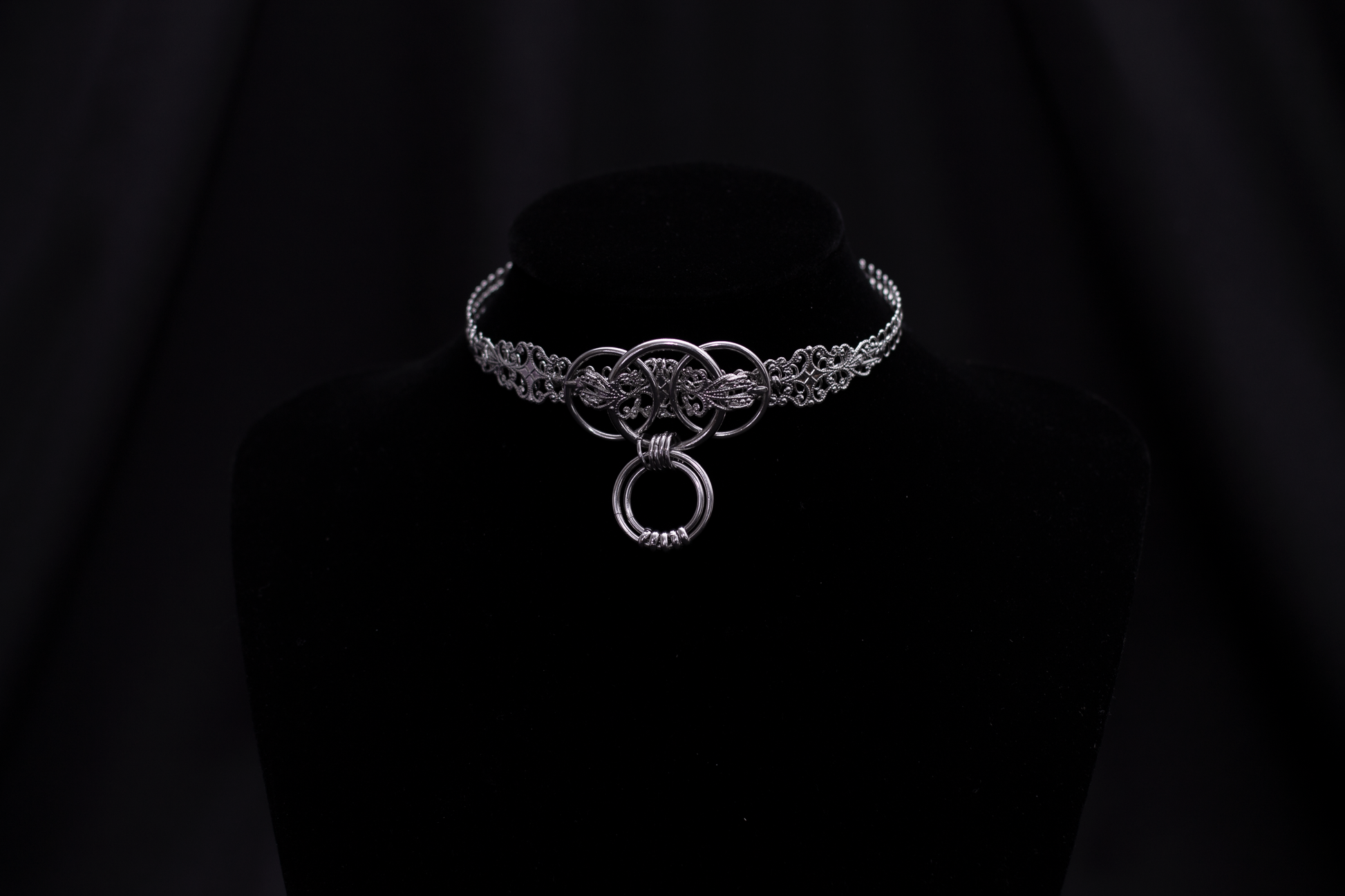 Elevate your accessory game with Myril Jewels' punk metal choker, featuring a prominent o-ring centerpiece. This exquisite piece, displayed on a black mannequin, combines intricate metalwork with a dark, polished finish, epitomizing the neo-goth aesthetic. It's an essential addition for anyone drawn to gothic-chic or witchcore styles, and versatile enough for everyday wear, Halloween, or as a standout piece for rave parties and festivals.