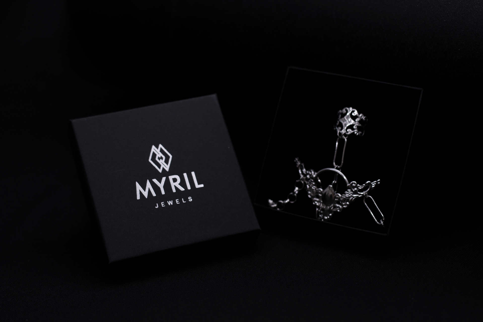 Myril Jewels presents a hand chain bracelet ring in its box, set against a black background, that combines neo-gothic intricacy with punk accents, perfect for avant-garde jewelry aficionados