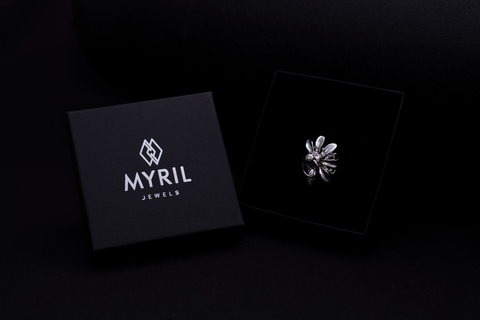 A sleek Myril Jewels presentation box with the brand's logo, accompanied by a polished Flower ring, exemplifies the luxurious dark-avantgarde style. Perfect for gothic and alternative fashion enthusiasts, this image highlights the brand's commitment to creating sophisticated, handcrafted Italian jewelry