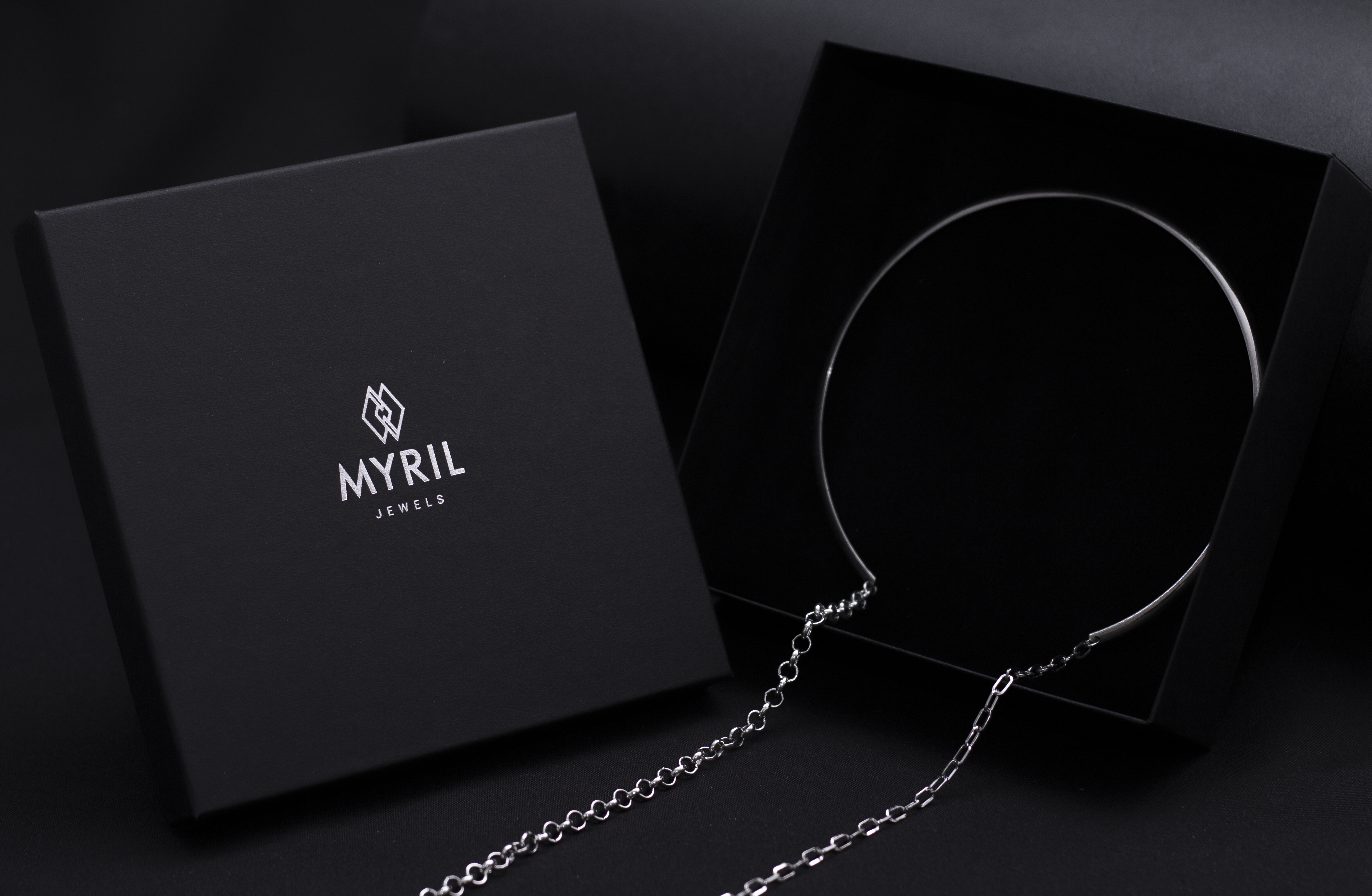 Elegant Myril Jewels packaging presents a sleek, rigid necklace with long hanging chains, reflecting a minimalist neo-goth style for the modern, dark-avantgarde enthusiast.