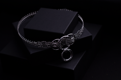 "Displayed against a black backdrop is a Myril Jewels punk metal choker, featuring an intricate silver filigree design and a prominent o-ring centerpiece. This choker exemplifies neo-goth craftsmanship, ideal for those who embrace a gothic-chic or dark-avantgarde style. It's a versatile accessory, perfect for Halloween, everyday wear, or as a statement piece for rave parties and festivals, embodying the edgy spirit of the Myril brand