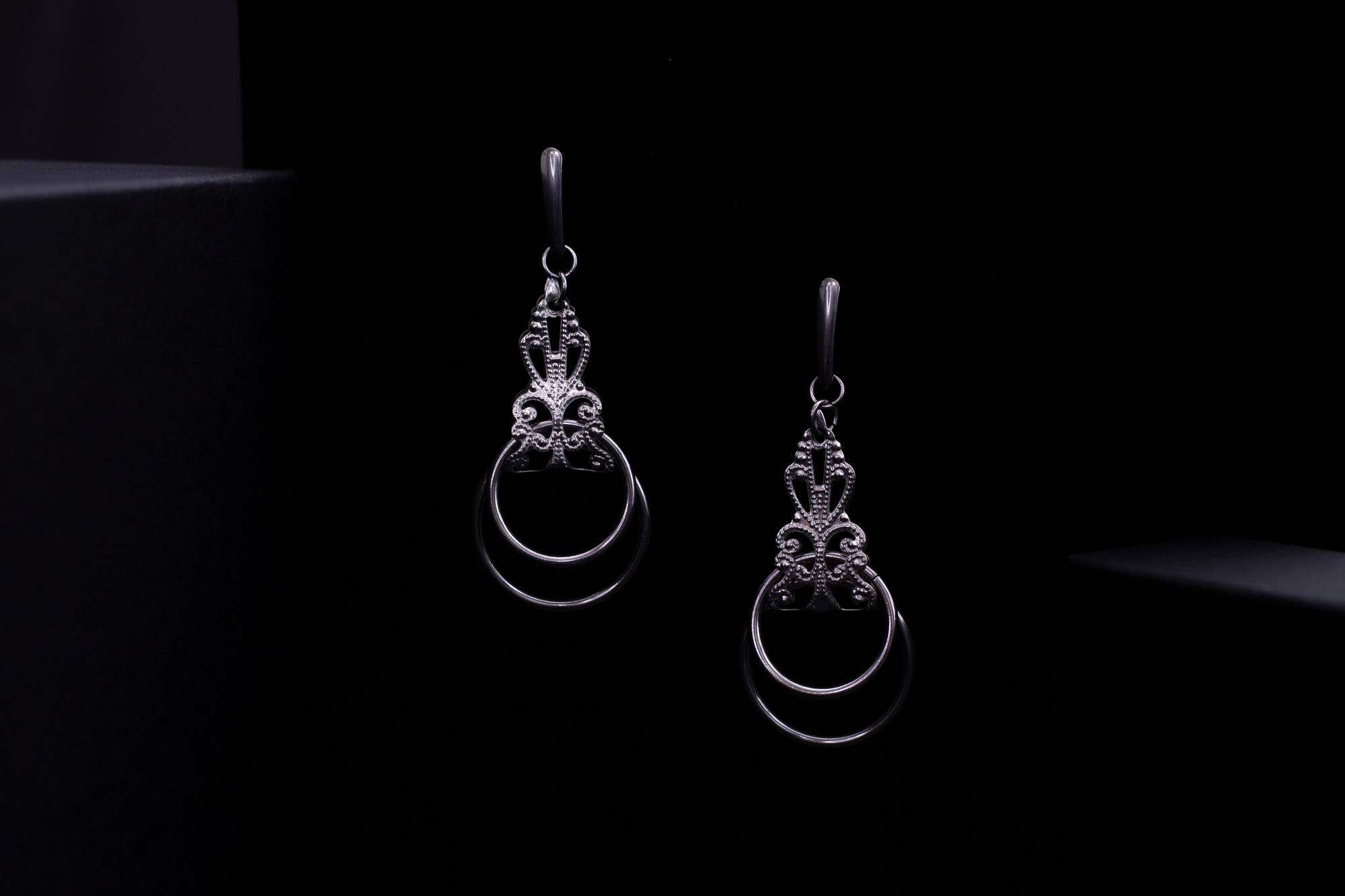 Myril Jewels presents a pair of stunning silver earrings, featuring an elaborate baroque design and hanging o-rings that exudes Neo Gothic charm, perfect for accentuating Gothic-chic and Witchcore styles. These earrings, exemplifying dark-avantgarde elegance, are a versatile choice for everyday wear as well as for special occasions like Halloween. The craftsmanship reflects the brand's commitment to unique, handmade jewelry for the alternative style lover.