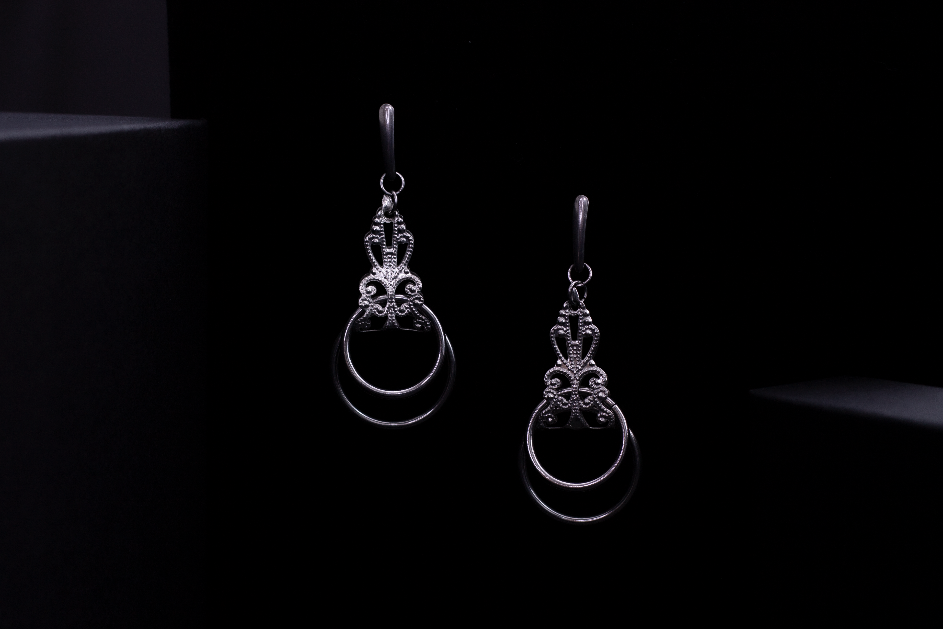 Myril Jewels presents a pair of stunning silver earrings, featuring an elaborate baroque design and hanging o-rings that exudes Neo Gothic charm, perfect for accentuating Gothic-chic and Witchcore styles. These earrings, exemplifying dark-avantgarde elegance, are a versatile choice for everyday wear as well as for special occasions like Halloween. The craftsmanship reflects the brand's commitment to unique, handmade jewelry for the alternative style lover.