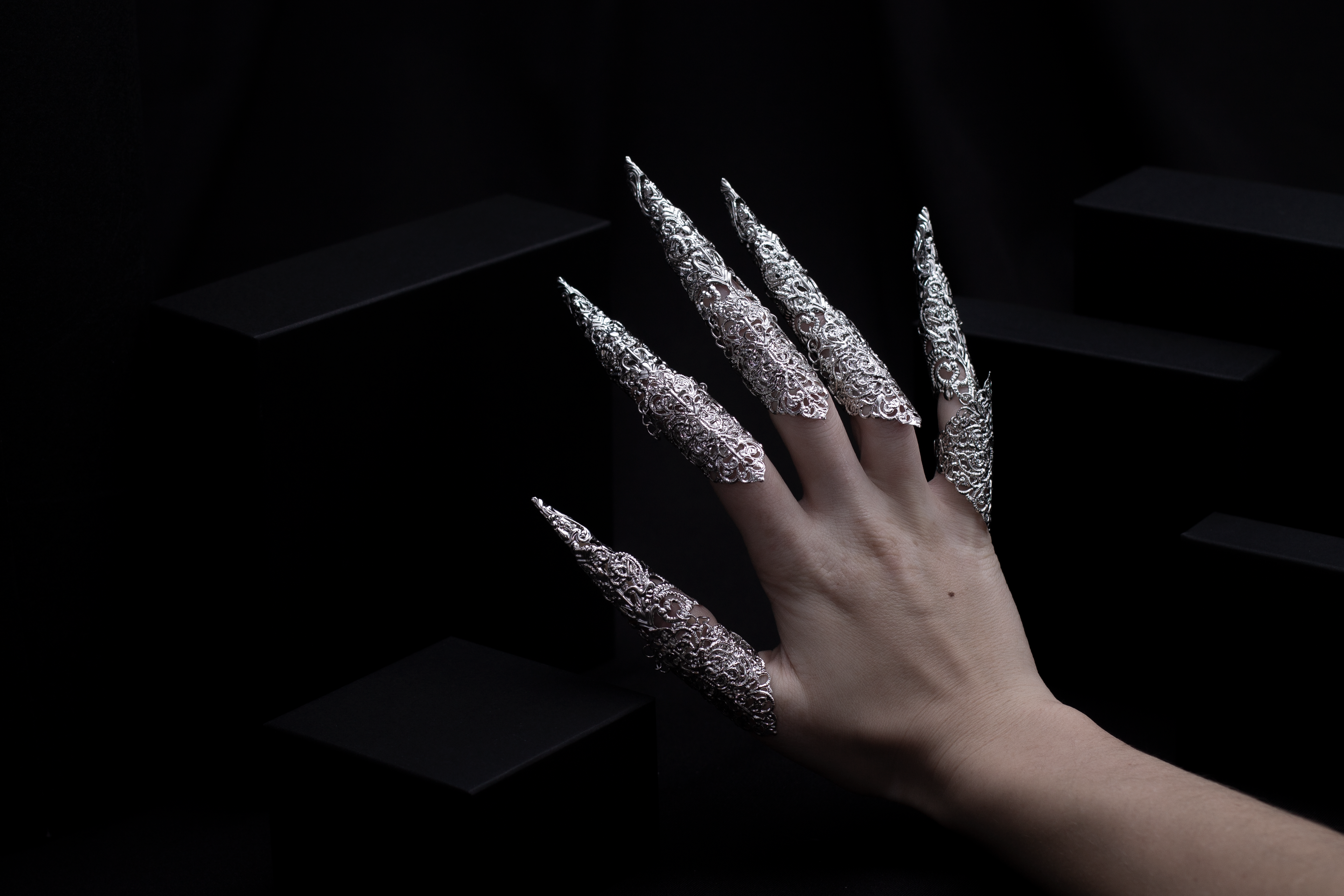 A hand emerges from the shadows, adorned with Myril Jewels' midi rings featuring elongated claws, capturing the essence of neo-gothic luxury. These finely crafted rings are a statement of dark avant-garde artistry, ideal for those who revel in gothic-chic and bold jewelry aesthetics.