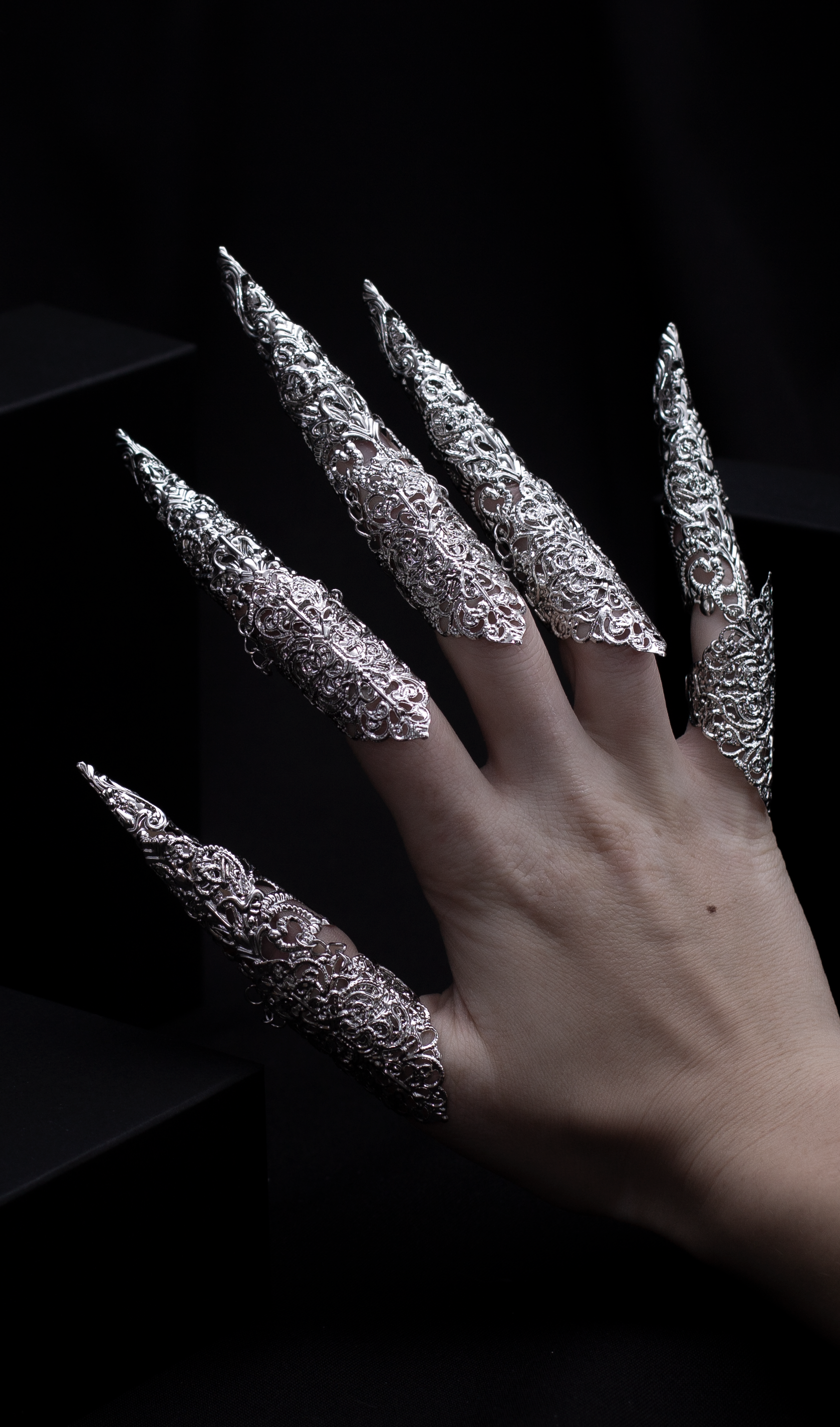 "A hand emerges from the shadows, flaunting Myril Jewels' midi rings with striking long claws, a perfect blend of neo-gothic flair and dark avant-garde elegance. This bold jewelry makes an ideal statement for Halloween, adding a touch of gothic-chic to any outfit.
