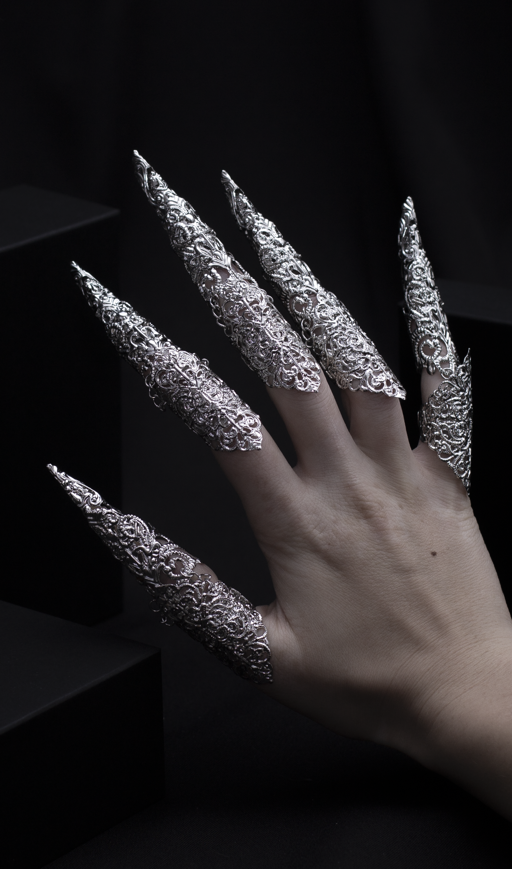 "A hand emerges from the shadows, flaunting Myril Jewels' midi rings with striking long claws, a perfect blend of neo-gothic flair and dark avant-garde elegance. This bold jewelry makes an ideal statement for Halloween, adding a touch of gothic-chic to any outfit.