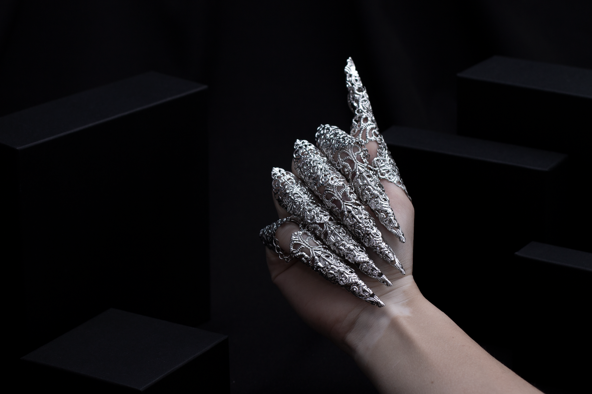 A hand emerges from the shadows, adorned with Myril Jewels' midi rings featuring elongated claws, capturing the essence of neo-gothic luxury. These finely crafted rings are a statement of dark avant-garde artistry, ideal for those who revel in gothic-chic and bold jewelry aesthetics.