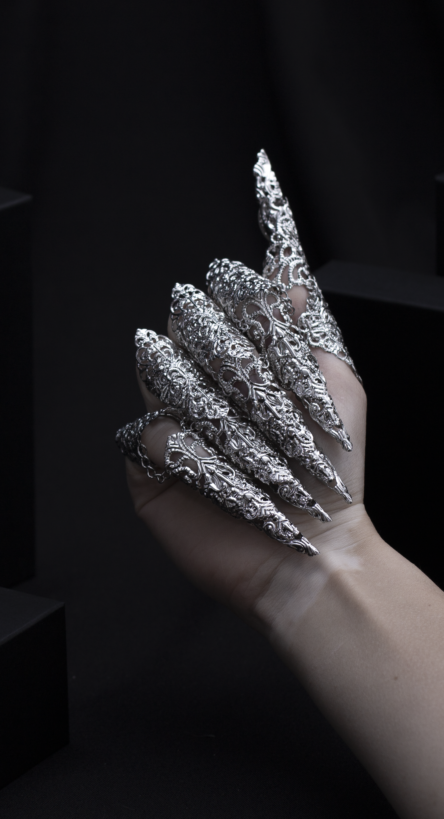 "A hand emerges from the shadows, flaunting Myril Jewels' midi rings with striking long claws, a perfect blend of neo-gothic flair and dark avant-garde elegance. This bold jewelry makes an ideal statement for Halloween, adding a touch of gothic-chic to any outfit.