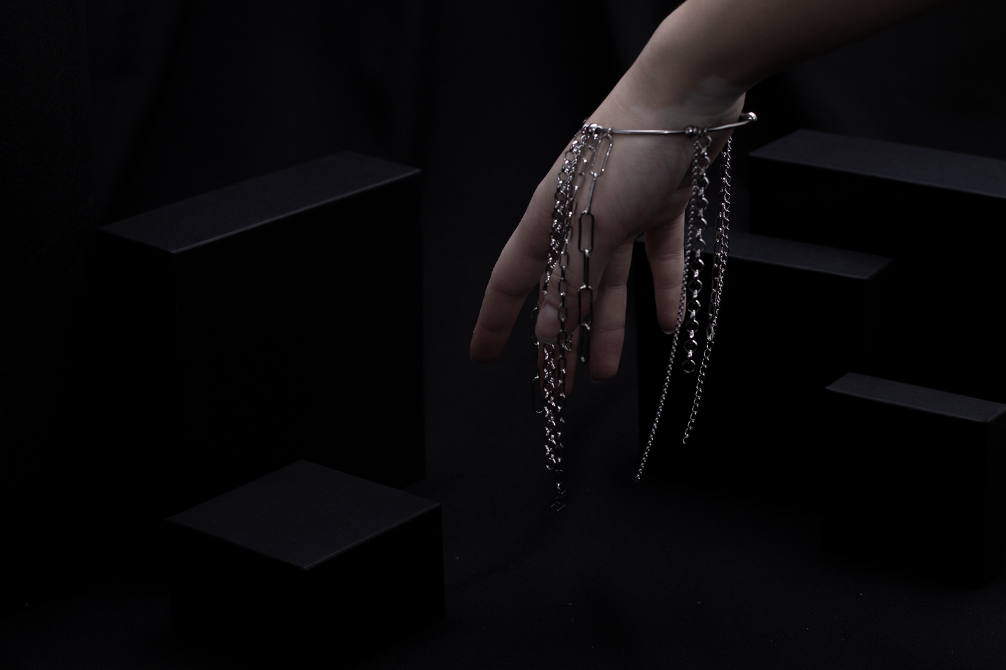 On a model’s wrist against a dark backdrop is a Myril Jewels rigid bracelet with hanging chains, reflecting a sleek neo-goth aesthetic. This stylish piece bridges the gap between boldness and minimalism, suitable for gothic, whimsigoth, and everyday wear, and perfect as a distinctive gift.