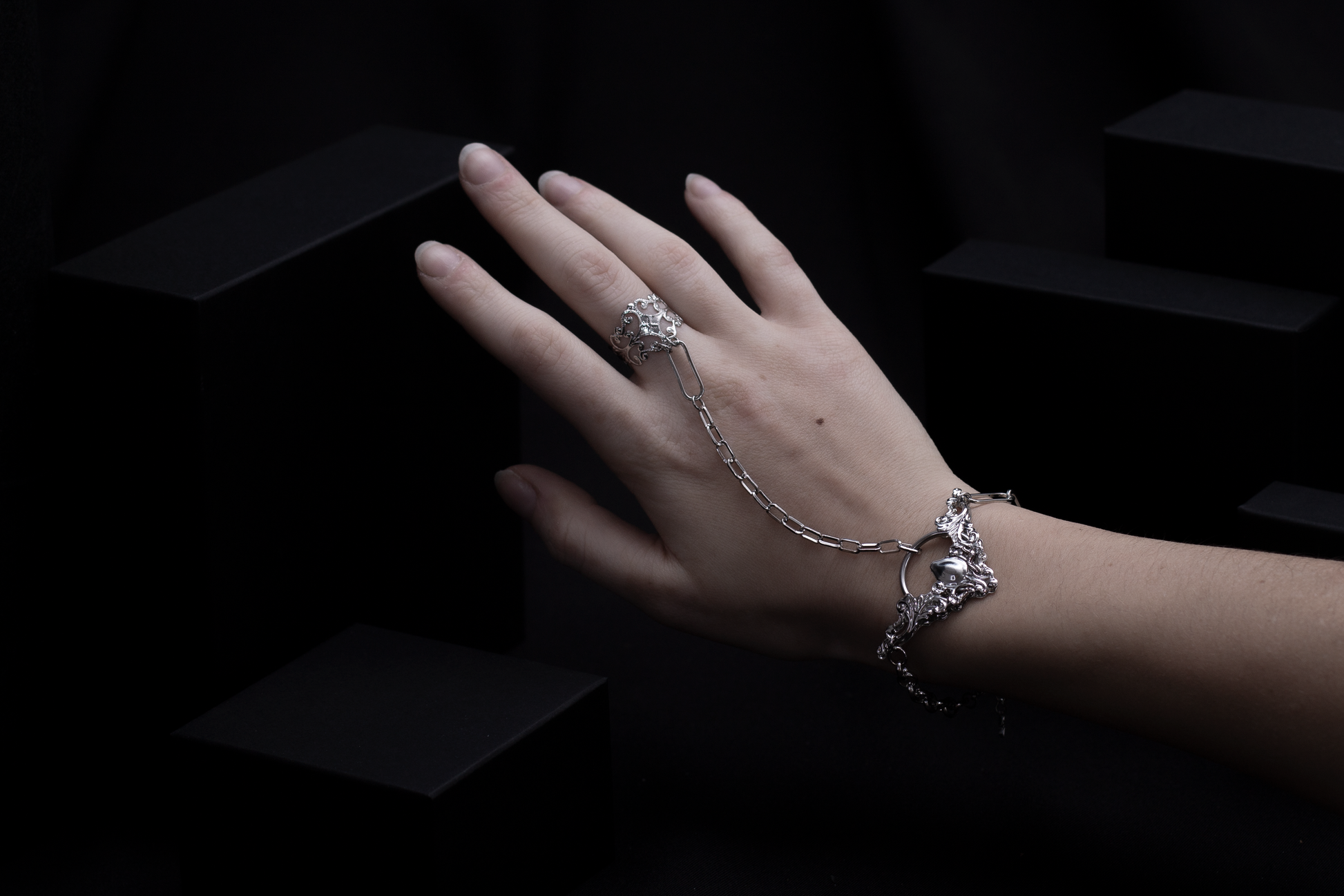 A pale hand adorned with a Myril Jewels hand chain bracelet ring, showcasing neo-gothic design. This elegant accessory, perfect for gothic and alternative style lovers, adds a touch of dark-avantgarde charm to any look, ideal for Halloween, rave parties, or as a unique gift for the goth girlfriend.