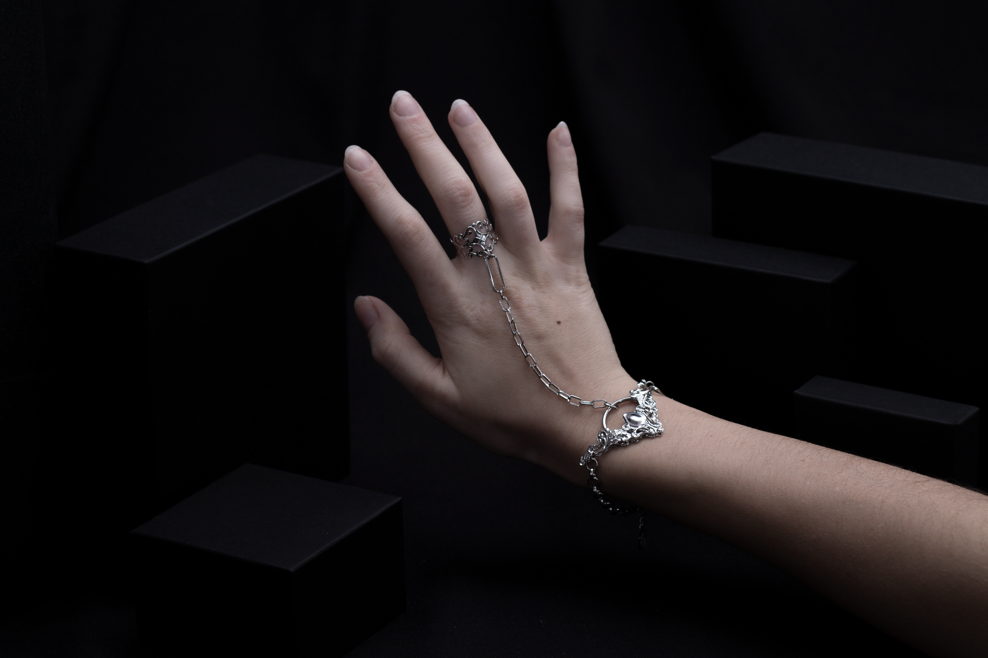 A graceful hand adorned with a Myril Jewels chain bracelet ring, featuring intricate neo-goth detailing, ideal for those seeking dark-avantgarde accessories with a witchcore edge.
