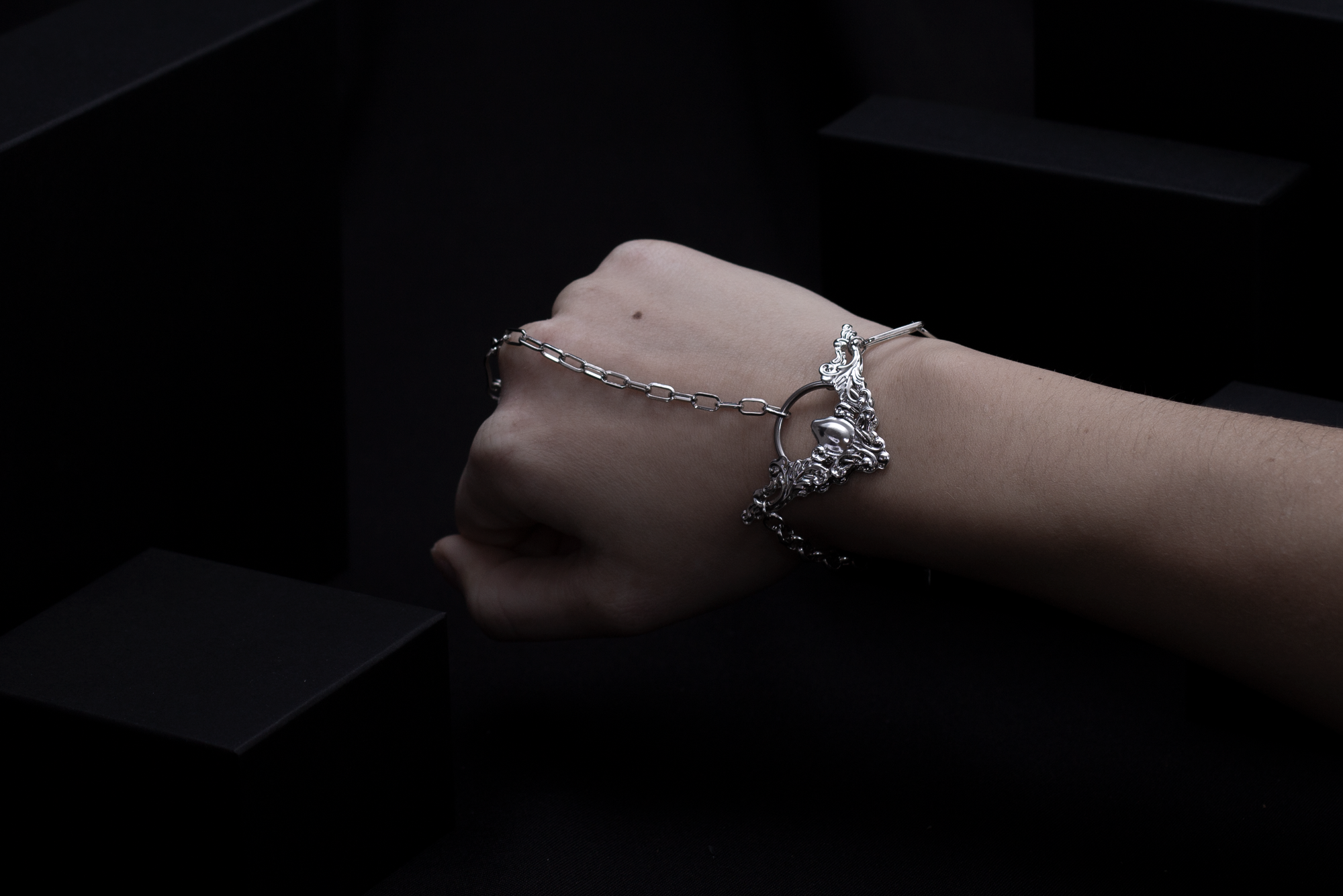 "Showcased is a Myril Jewels hand chain bracelet ring, an elegant neo-goth piece combining intricate filigree with a stylish chain that drapes over the hand.