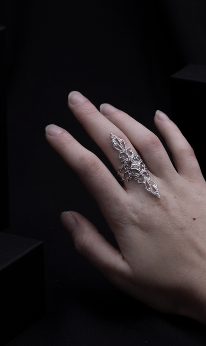 A woman's hand elegantly displaying a silver filigree full-finger ring against a dark background with geometric shapes, embodying a sophisticated gothic style.
