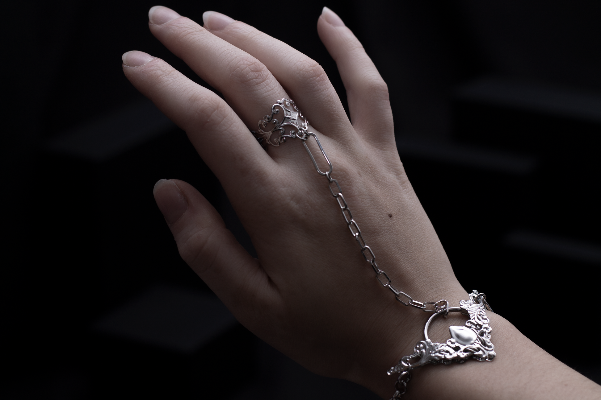 A hand displays a Myril Jewels hand chain bracelet ring, embodying a dark avant-garde aesthetic. The delicate chain links to a detailed filigree ring, capturing the neo-goth spirit perfect for Halloween, everyday wear, or as a unique piece for goth-inspired ensembles.