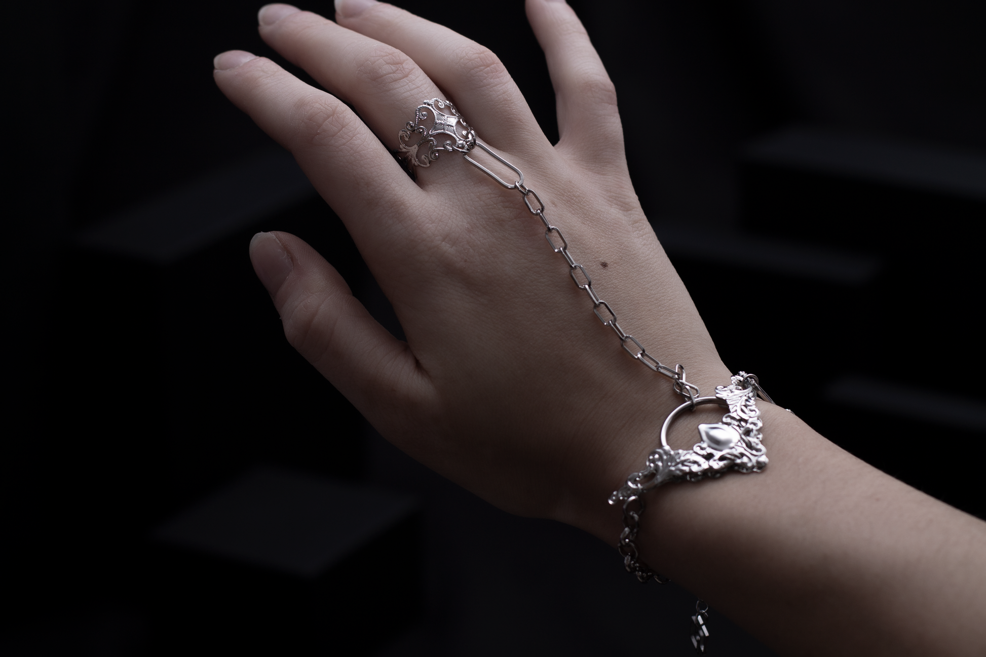 A graceful hand adorned with a Myril Jewels hand chain bracelet ring, showcasing neo-gothic elegance. The intricate design captures a dark-avantgarde essence, perfect for gothic and alternative styles, and is versatile for everyday wear, festival fashion, or as a unique gift for a goth girlfriend.