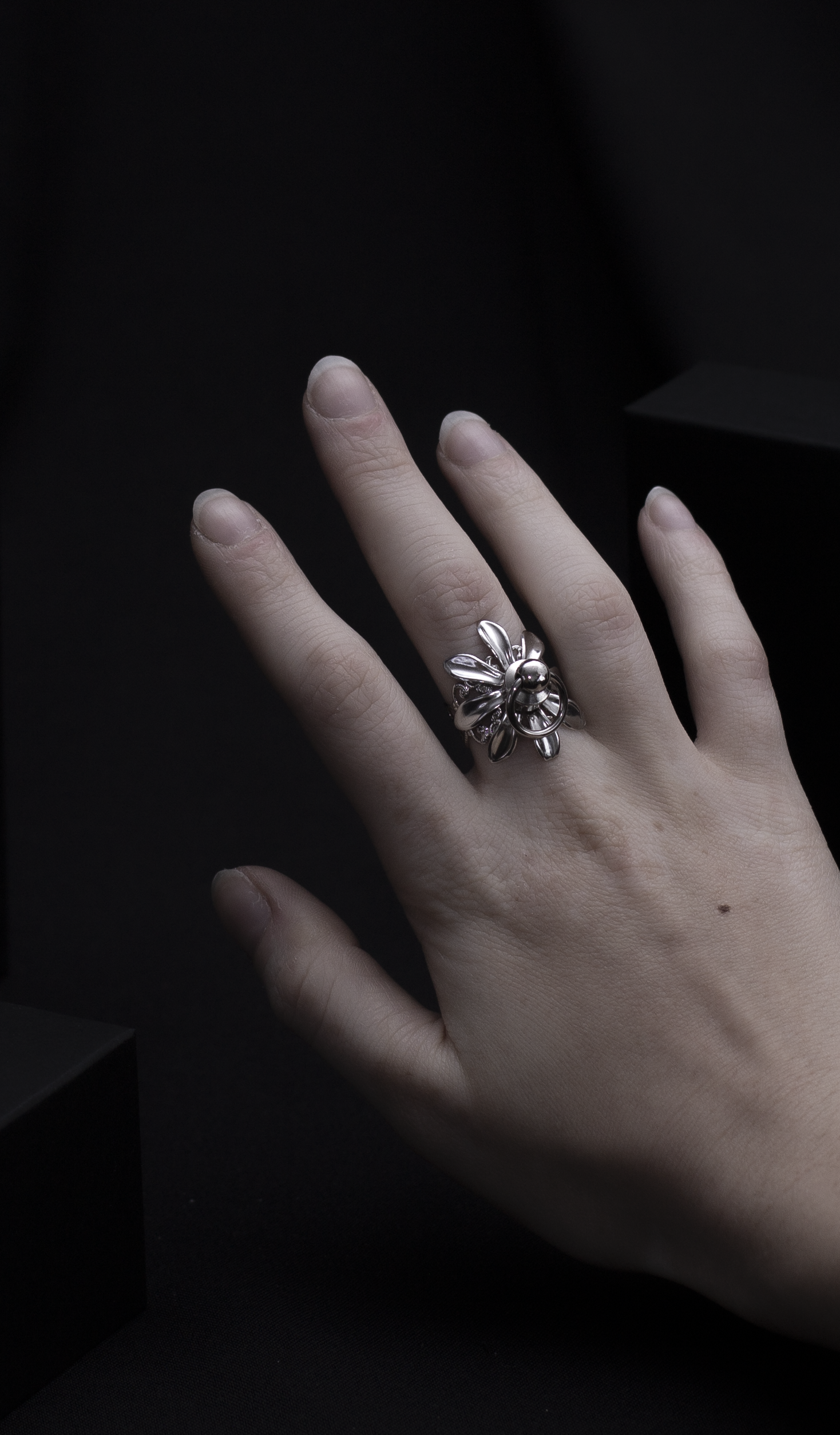 A solitary hand displays a Myril Jewels flower ring with o-ring stud in the middle, a masterpiece of dark-avantgarde jewelry with a punk twist. The ring's silver sheen and intricate floral design embody the luxurious, gothic aesthetic, a signature of Myril Jewels, catering to those with a penchant for bold, alternative fashion.