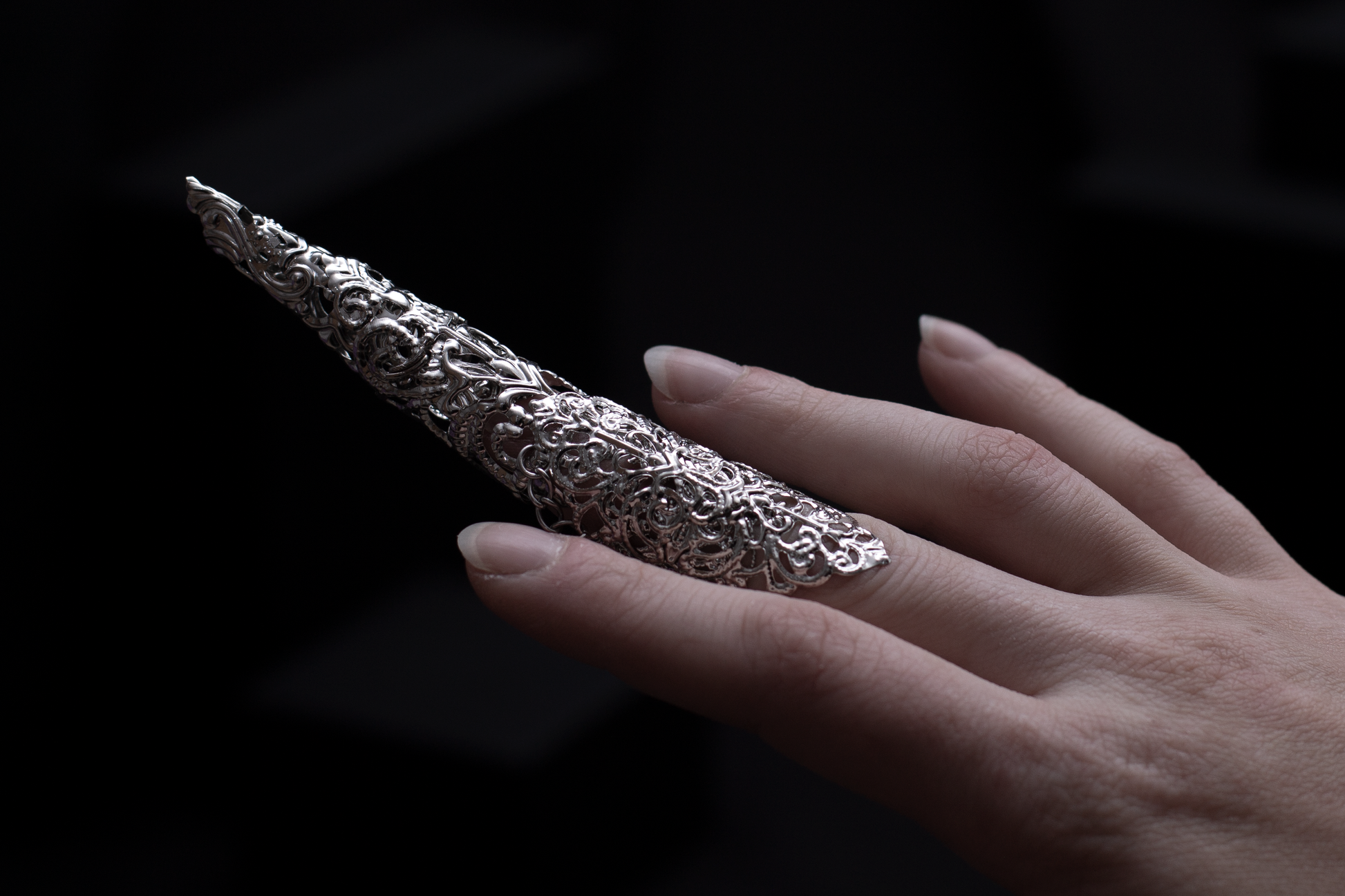 A hand emerges from the shadows, adorned with Myril Jewels' striking midi ring featuring long, intricate claw. This neo-gothic masterpiece perfectly complements a dark avant-garde look, ideal for those seeking bold, Halloween-inspired gothic-chic jewelry.