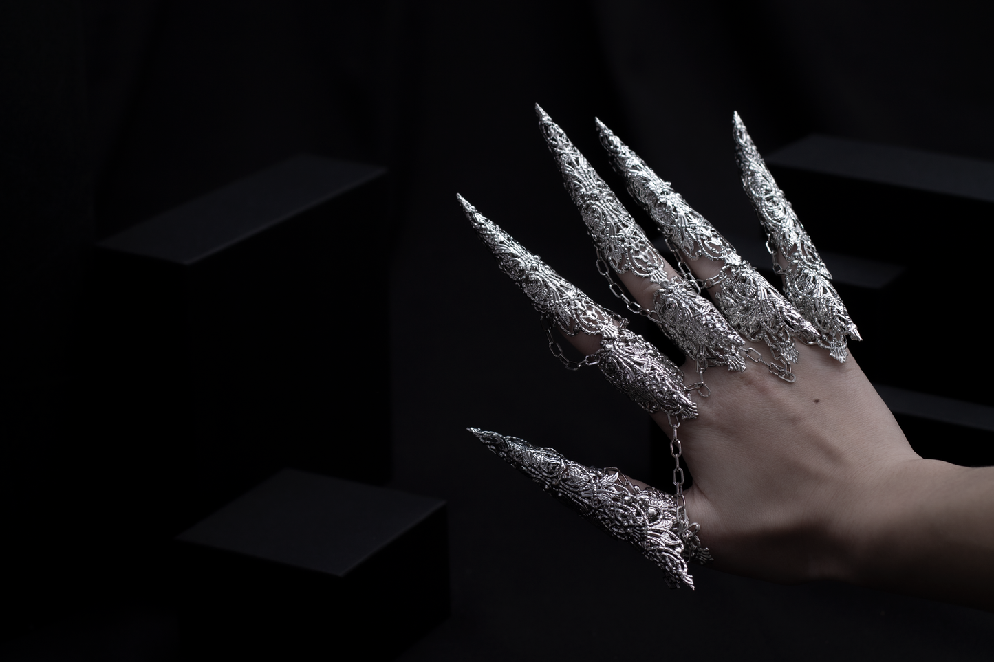 A hand is strikingly adorned with a set of Myril Jewels' dragon-like long claw rings, casting a neo-gothic spell. This bold jewelry, embodying the essence of dark avant-garde, is a dream for gothic style enthusiasts, making it an ideal choice for Halloween or as a unique gift.