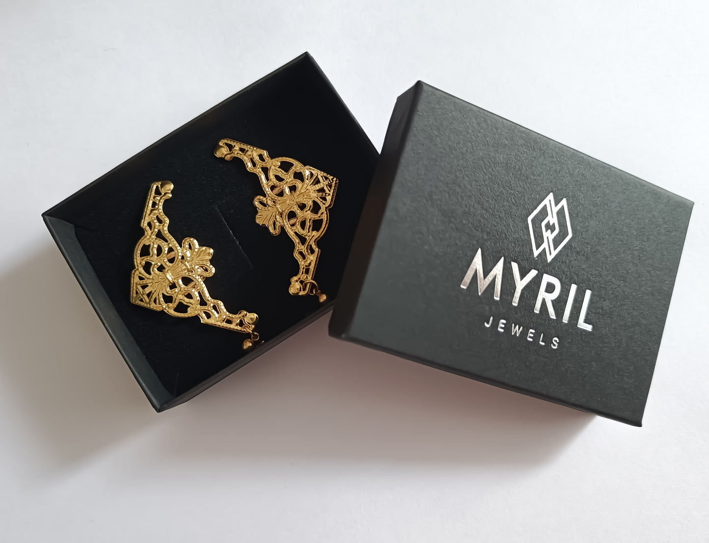 nside a sleek black Myril Jewels box lies a pair of exquisite gold cuff earrings, showcasing the intricate craftsmanship synonymous with the neo-goth brand. These ornate pieces, with their elaborate filigree design, exude a dark-avantgarde elegance, perfect for anyone who embraces gothic-chic or whimsigoth style. Ideal for adding a touch of witchcore to everyday wear or as a standout accessory for rave parties and festivals