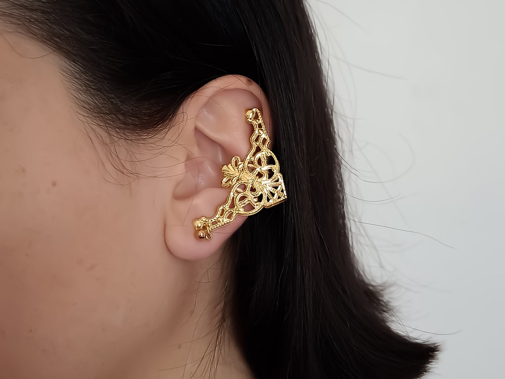 A close-up view of a model wearing Myril Jewels' gold cuff earrings, which are masterfully crafted in a rich gold tone. The detailed filigree design evokes a neo-gothic aesthetic, perfect for those who desire a touch of dark-avantgarde elegance. These gold earrings are ideal for gothic-chic fashion lovers, adding a unique statement to both everyday wear and special occasions like Halloween, and are versatile enough for festival adornment or as part of a minimal goth wardrobe.