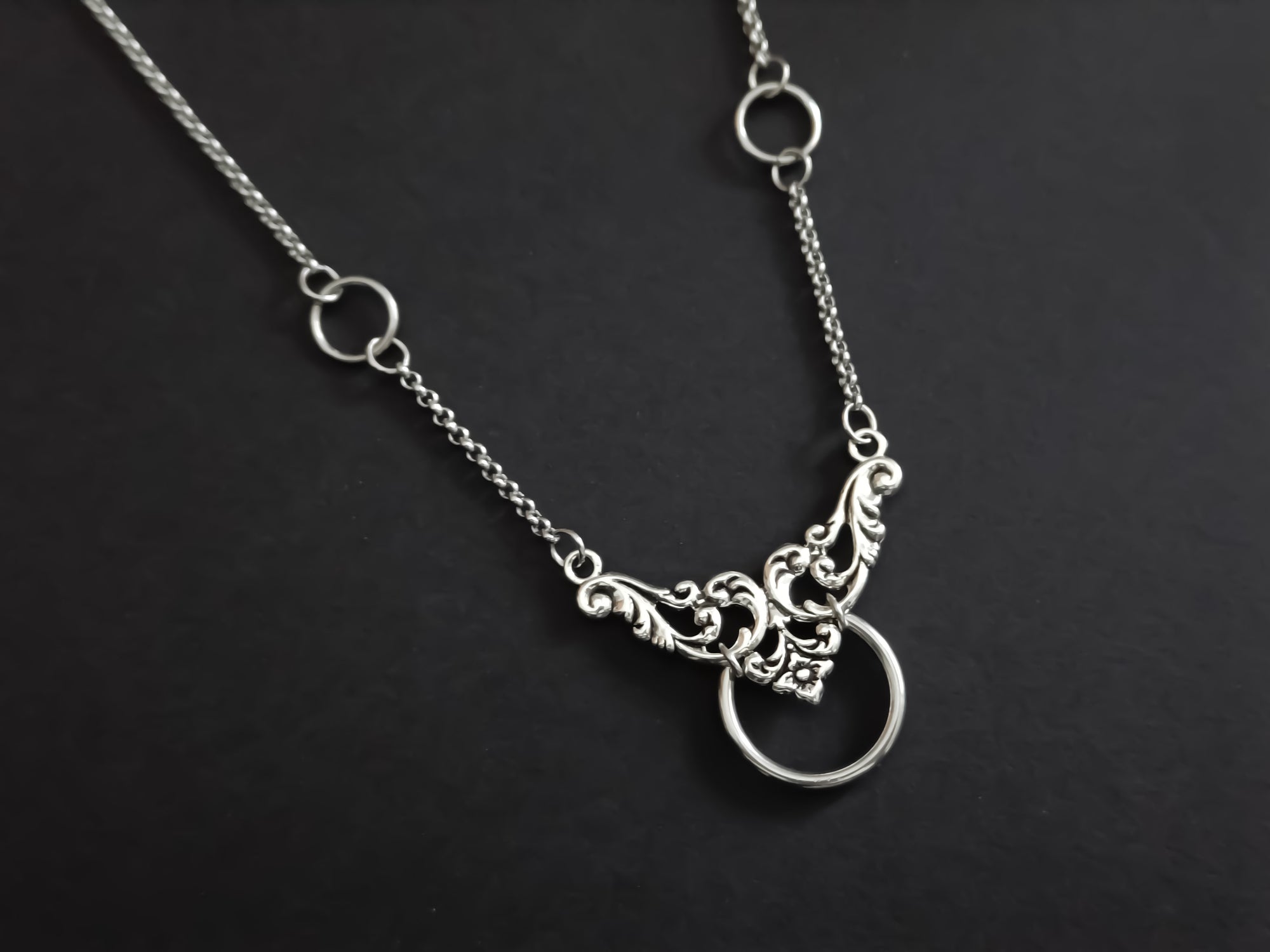 An elegant Myril Jewels chain choker with a floral motif and central O-ring, merging neo-goth style with dark-avantgarde sophistication, suitable for various occasions from everyday wear to special events