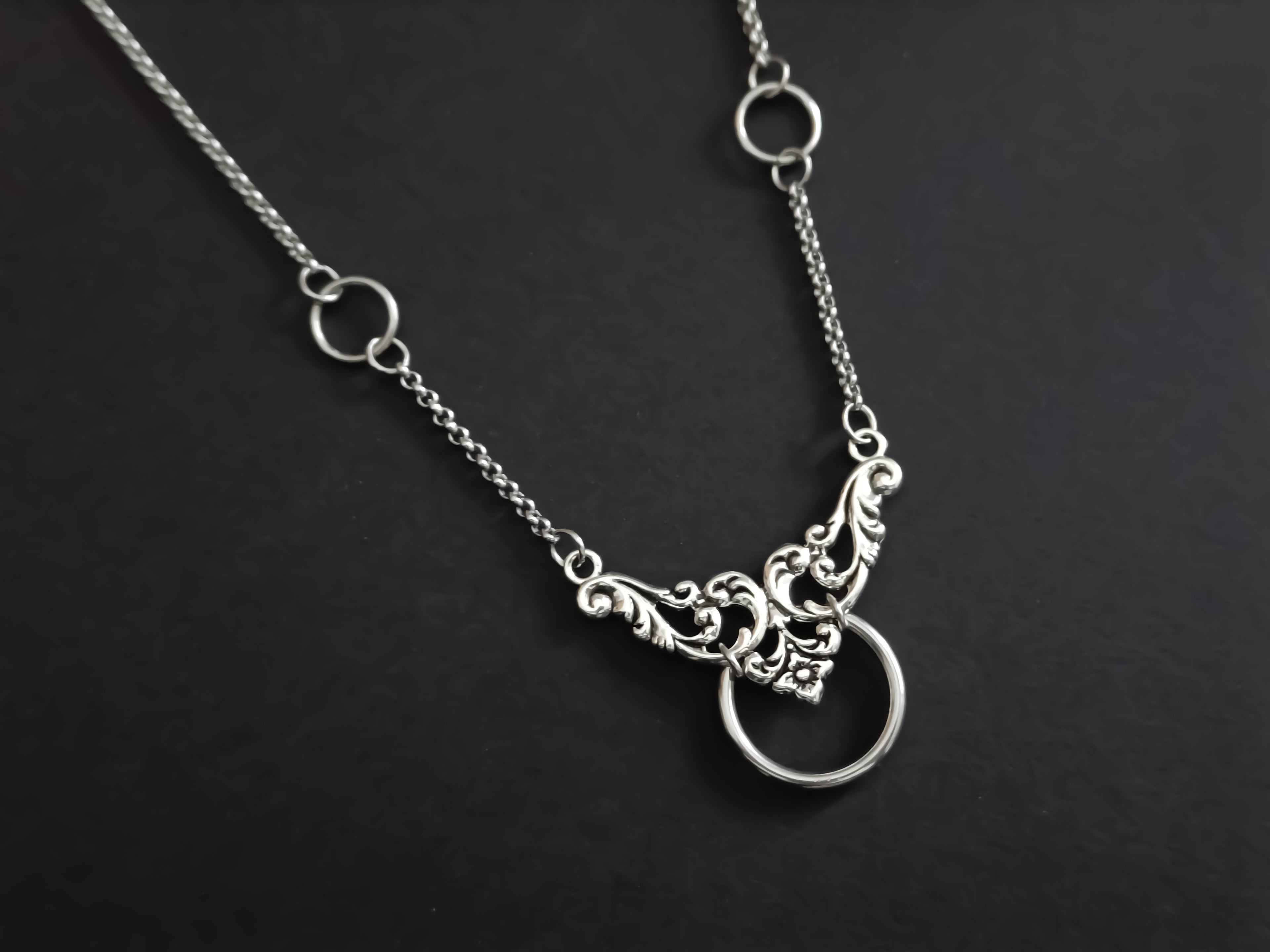An elegant Myril Jewels chain choker with a floral motif and central O-ring, merging neo-goth style with dark-avantgarde sophistication, suitable for various occasions from everyday wear to special events