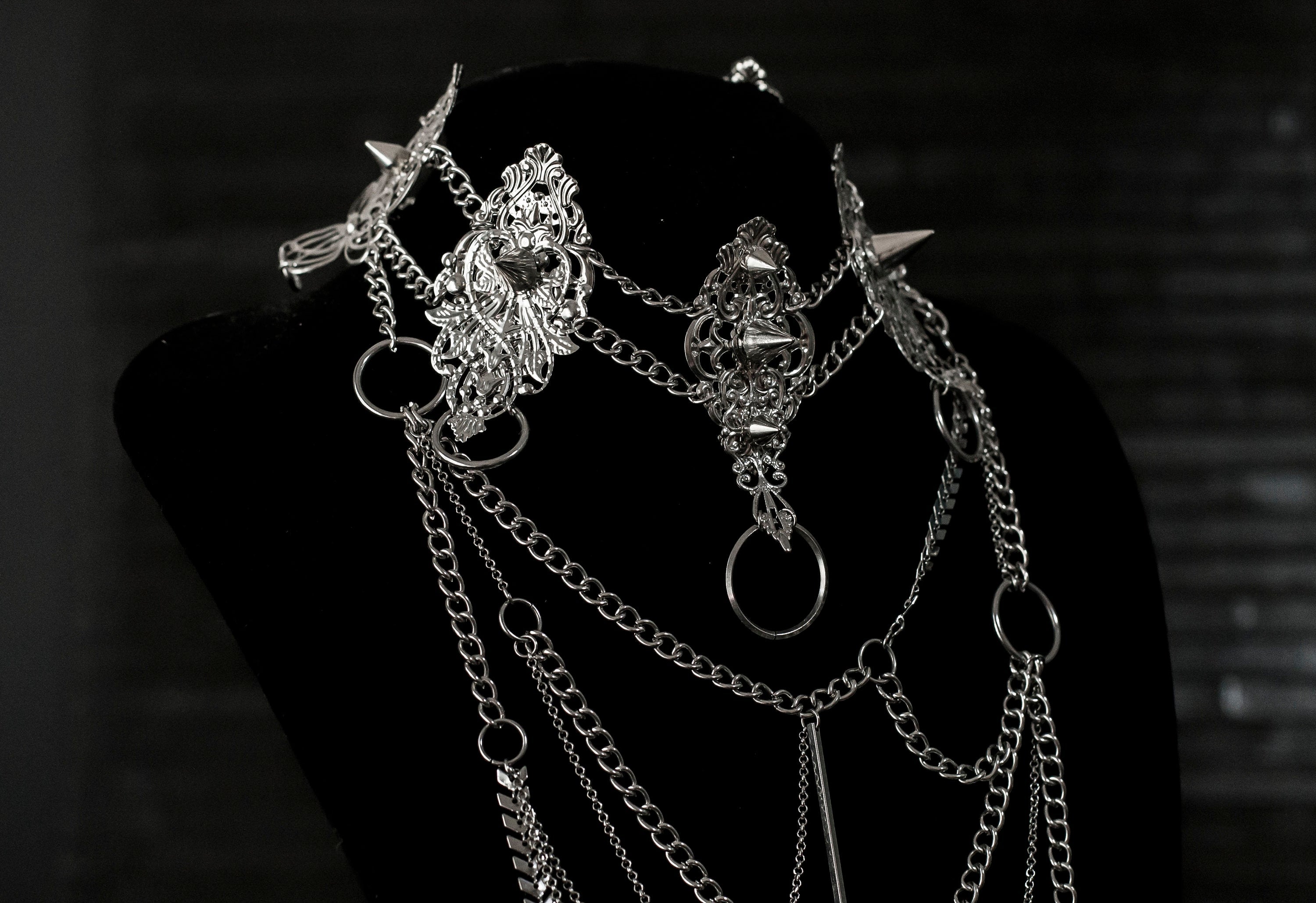 Myril Jewels presents an exquisite punk studded metal choker paired with a multi-layer long chain necklace, embodying the dark avant-garde spirit. This Italian handcrafted ensemble is a testament to the fusion of Neo Gothic flair and Gothic-chic, perfect for Halloween, everyday wear, or any whimsigoth and witchcore inspired look. The layered chains add depth to the minimal goth aesthetic, making it a versatile statement piece for alternative style connoisseurs