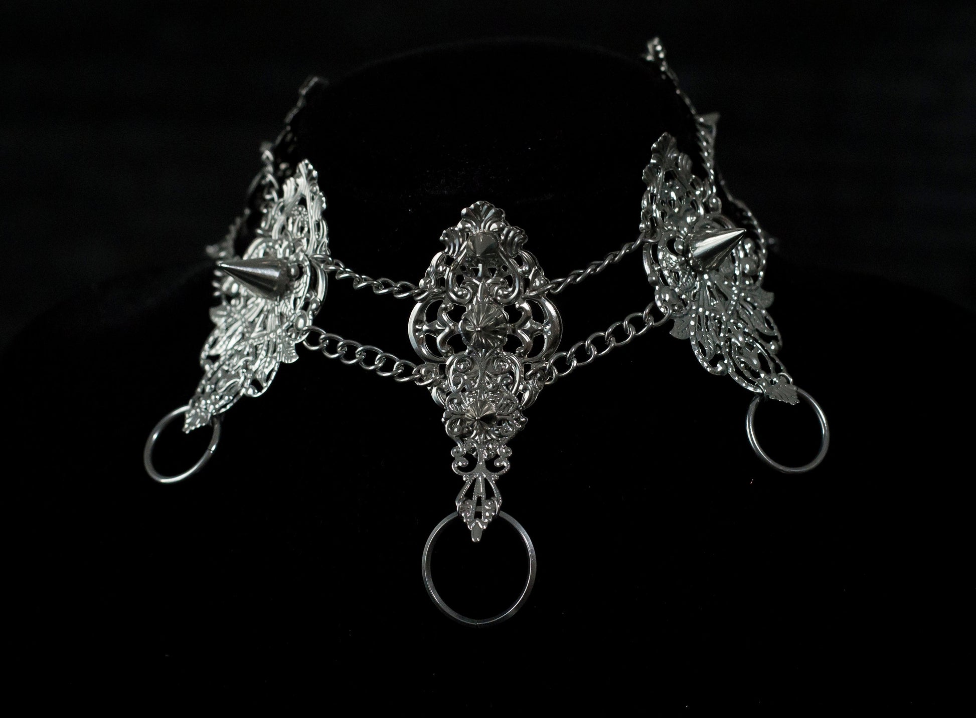This Myril Jewels dark avant-garde metal choker, featuring punk studded details, is an exquisite piece for gothic fashion aficionados. Its intricate filigree and chain design showcase the brand's commitment to handcrafted Neo Gothic elegance. Ideal for Gothic Lolita, Gothic-chic, or whimsigoth wardrobes, it's a statement accessory for Halloween and everyday minimal goth style, exuding witchcore vibes