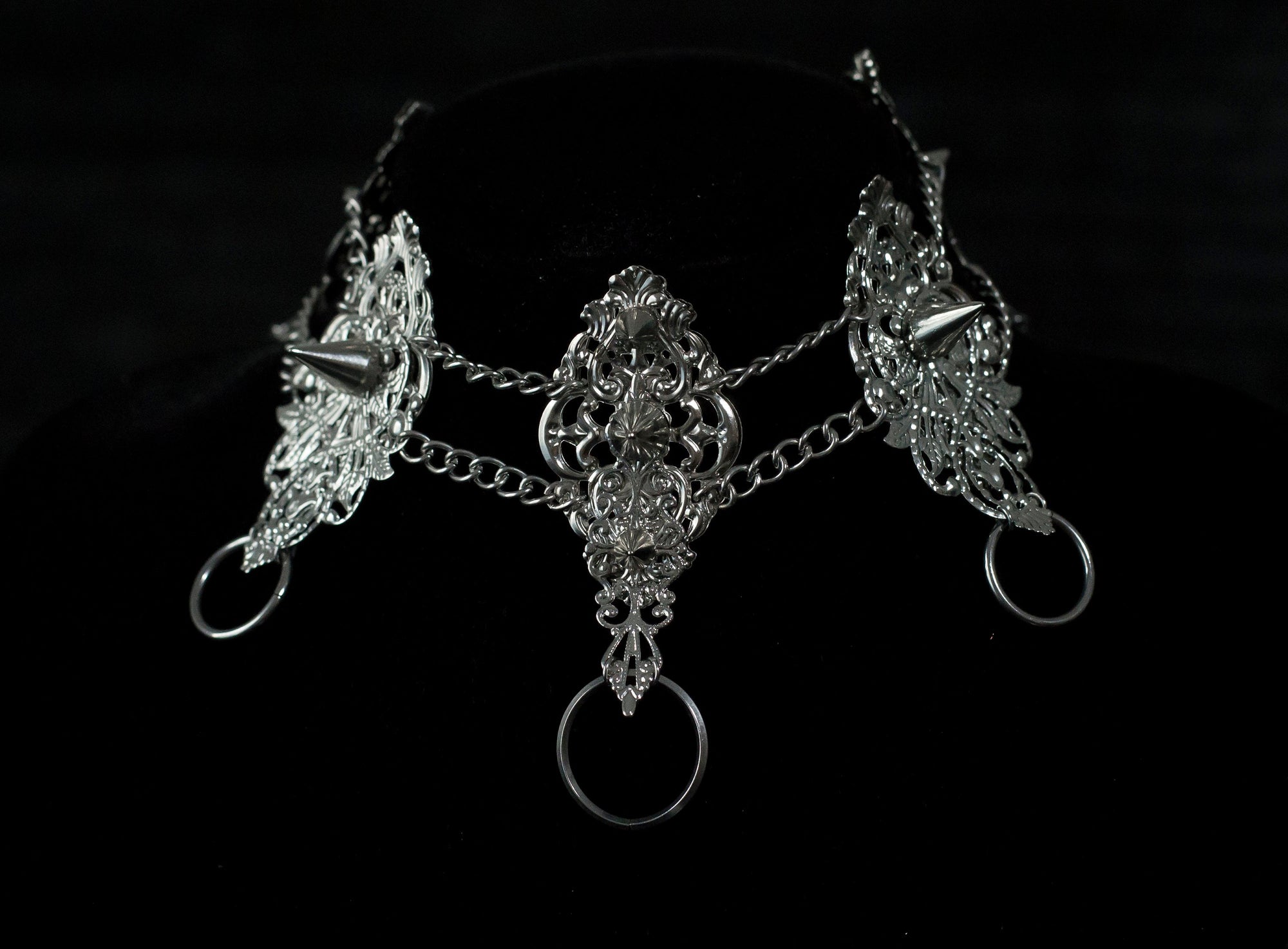 This Myril Jewels dark avant-garde metal choker, featuring punk studded details, is an exquisite piece for gothic fashion aficionados. Its intricate filigree and chain design showcase the brand's commitment to handcrafted Neo Gothic elegance. Ideal for Gothic Lolita, Gothic-chic, or whimsigoth wardrobes, it's a statement accessory for Halloween and everyday minimal goth style, exuding witchcore vibes